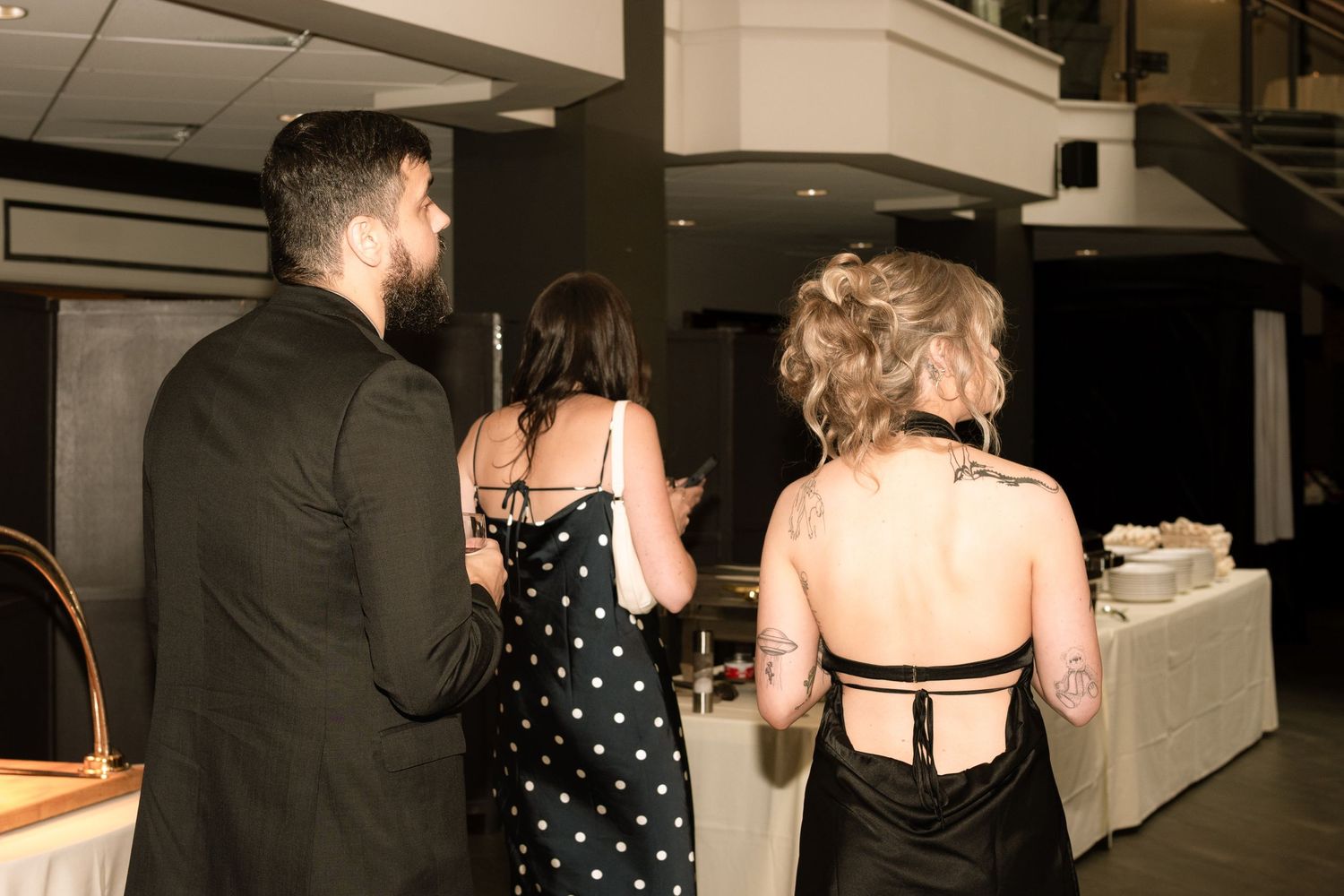 People chat and interact at an indoor social event, with black formal attire and mood lighting visible.