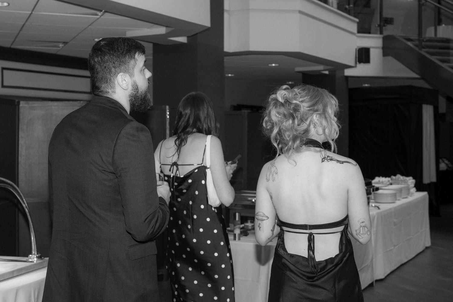 A black and white photo showing people in formal attire standing in line at what appears to be an indoor event.