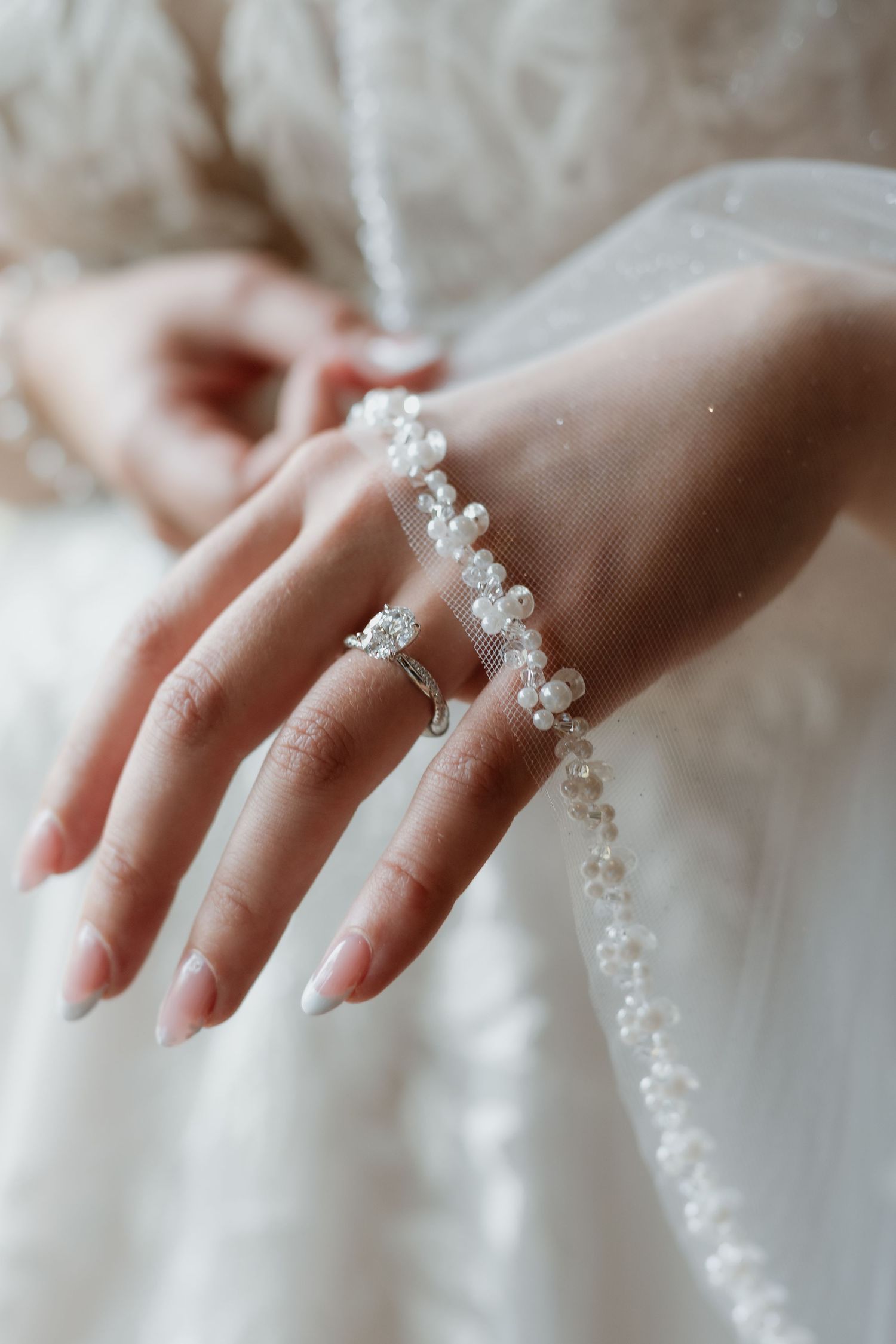 Delicate pearl and crystal beaded jewelry adorns elegant hands against a soft white fabric background.