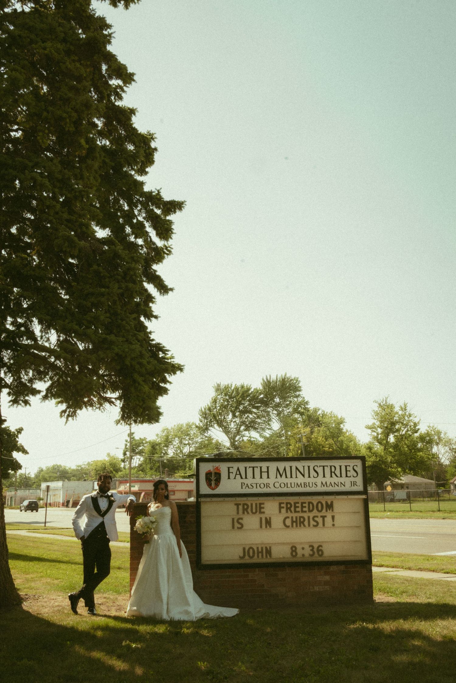 Newlywed couple posing by Faith Ministries church sign reading True Freedom Is In Christ, John 8:36.