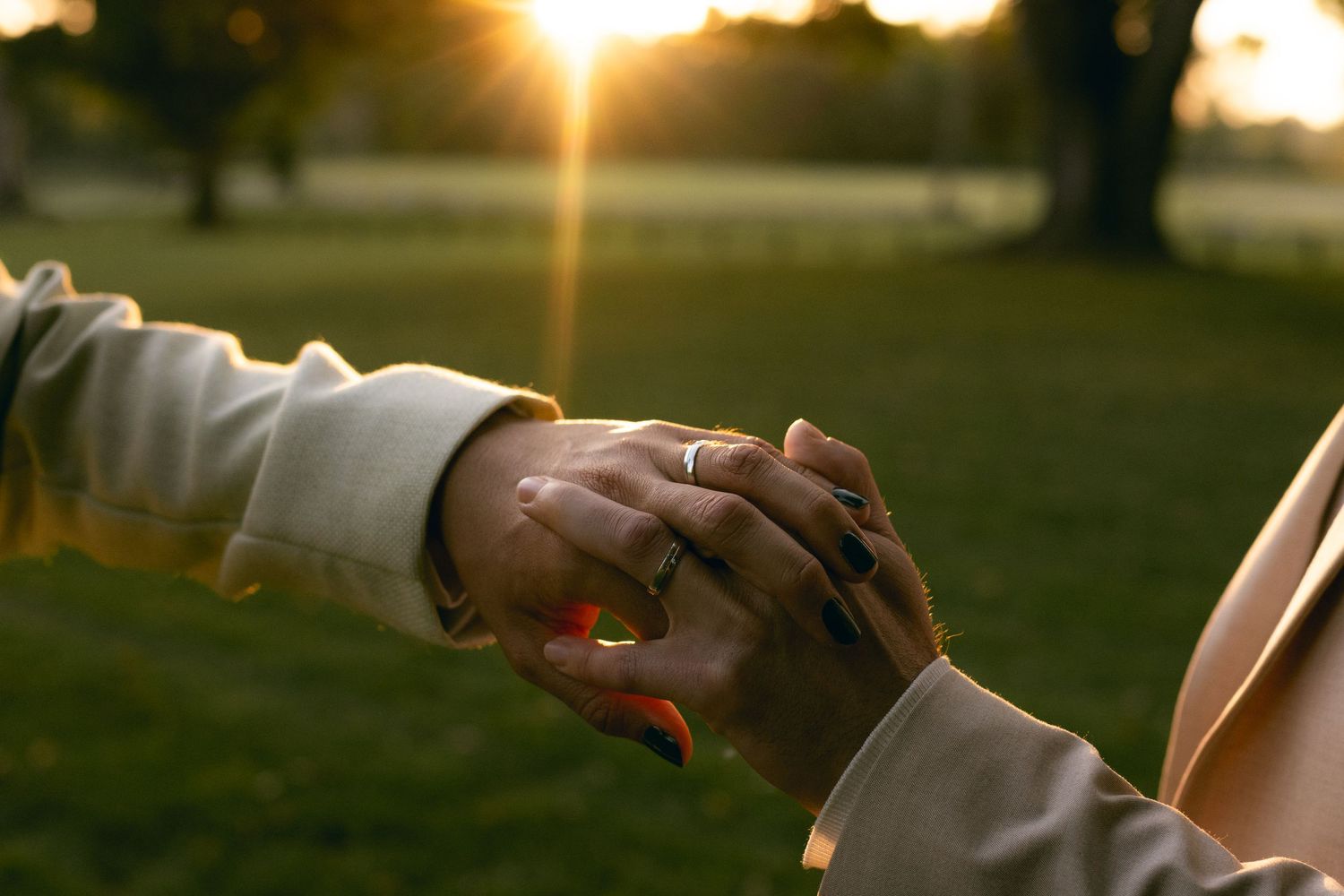 A couple holds hands during golden hour sunset in a romantic outdoor setting.