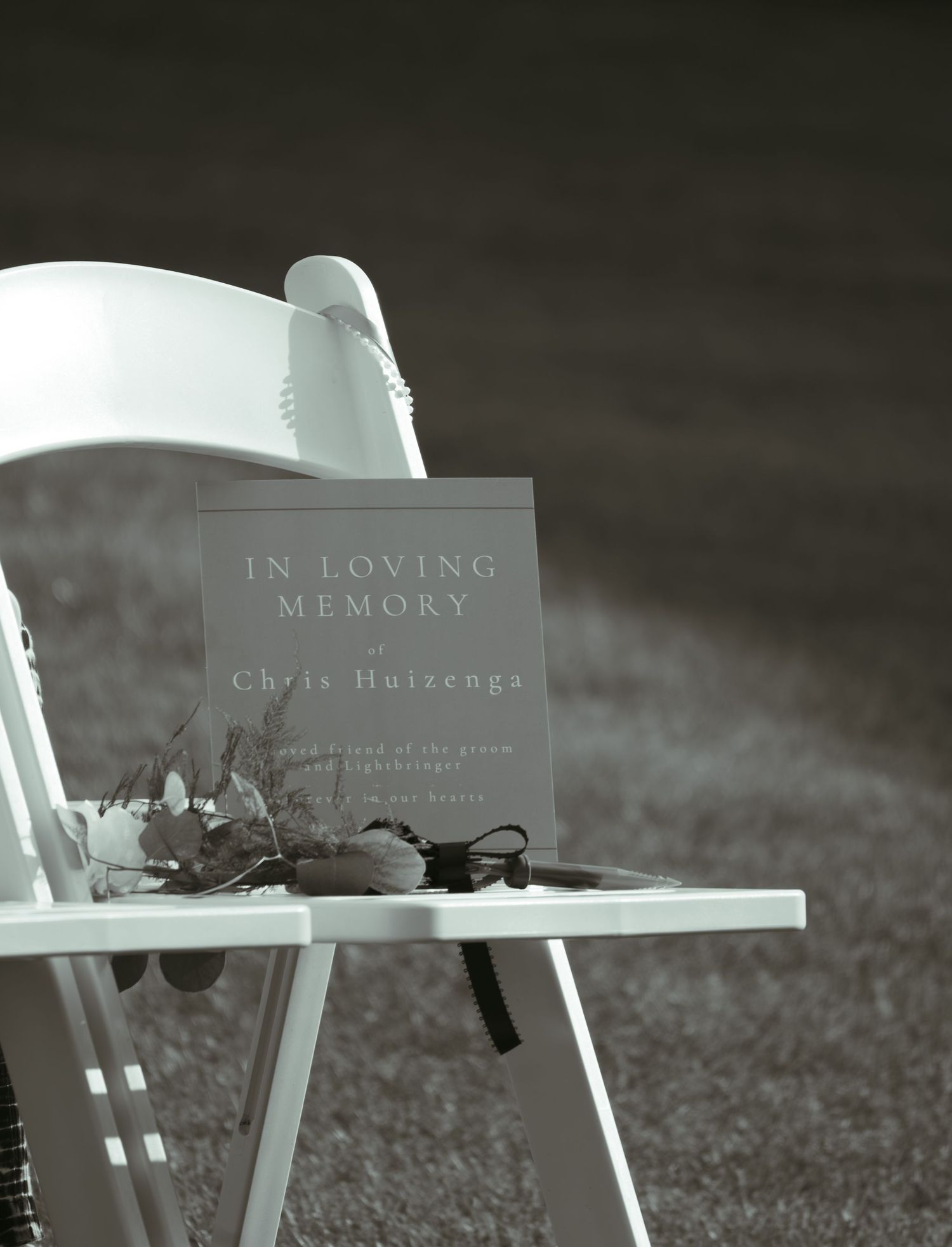 White memorial chairs with 'In Loving Memory' plaques arranged at an outdoor wedding ceremony.