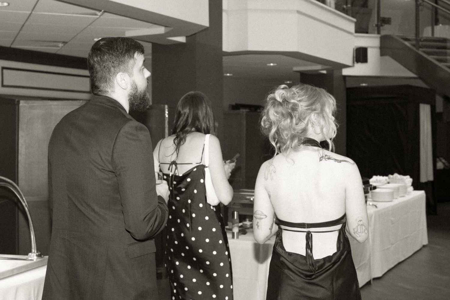 A vintage black and white photo showing people in formal attire at a social gathering from behind.