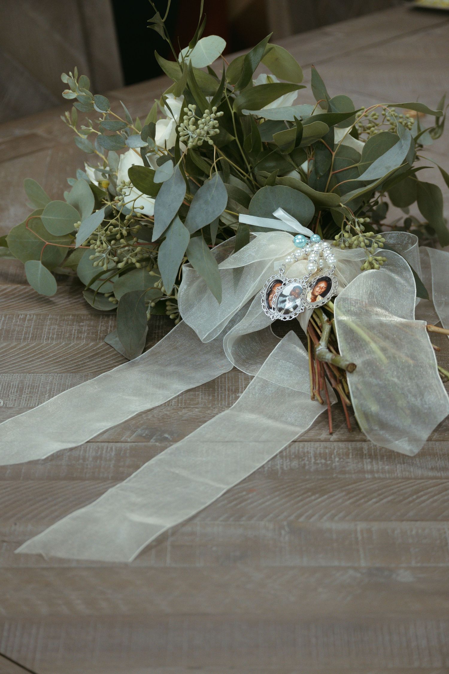 A wedding bouquet with eucalyptus leaves and white ribbon lying on a wooden surface.