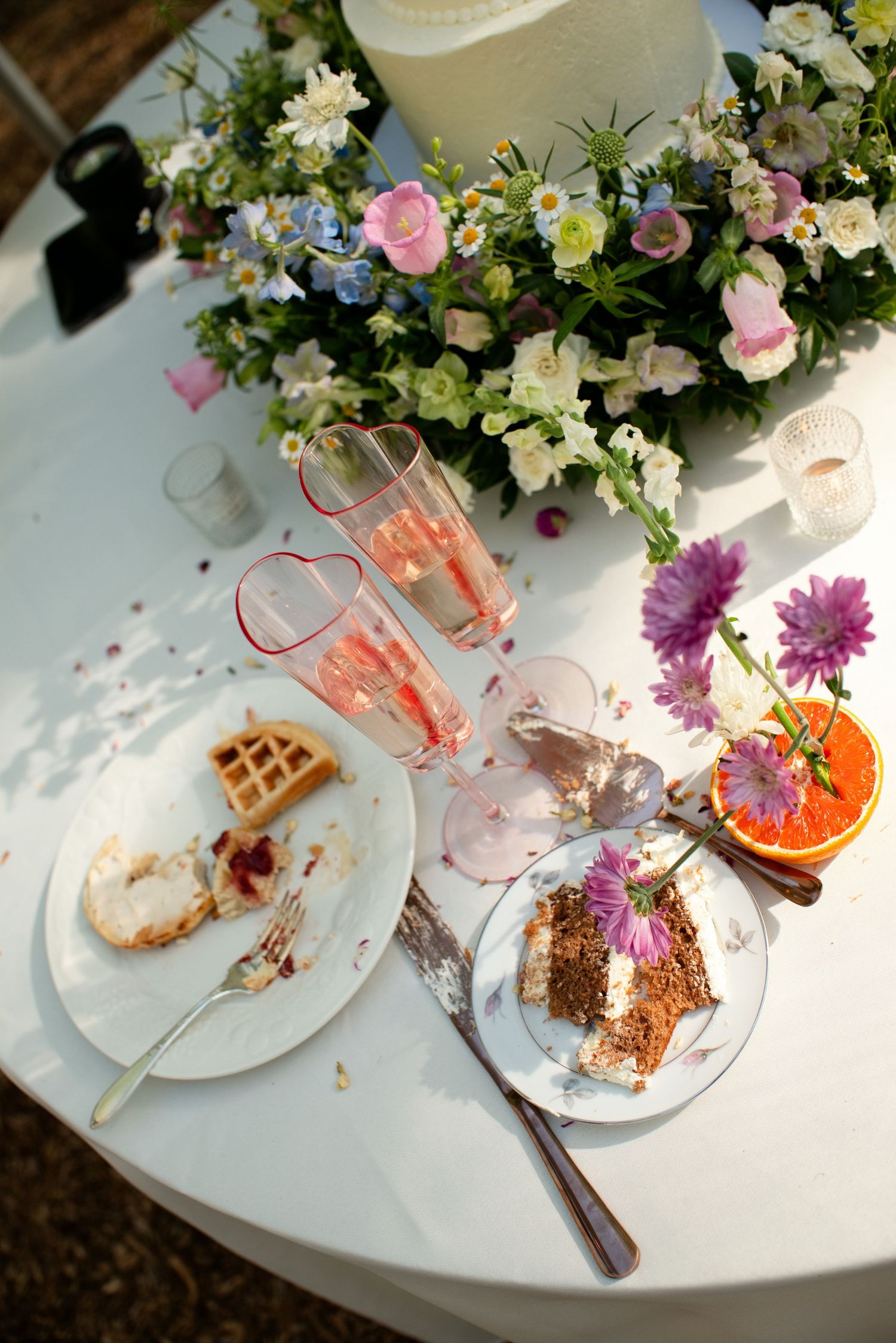 Wedding table with champagne flutes, cake slices, waffle, and floral arrangements featuring pink and white blooms.