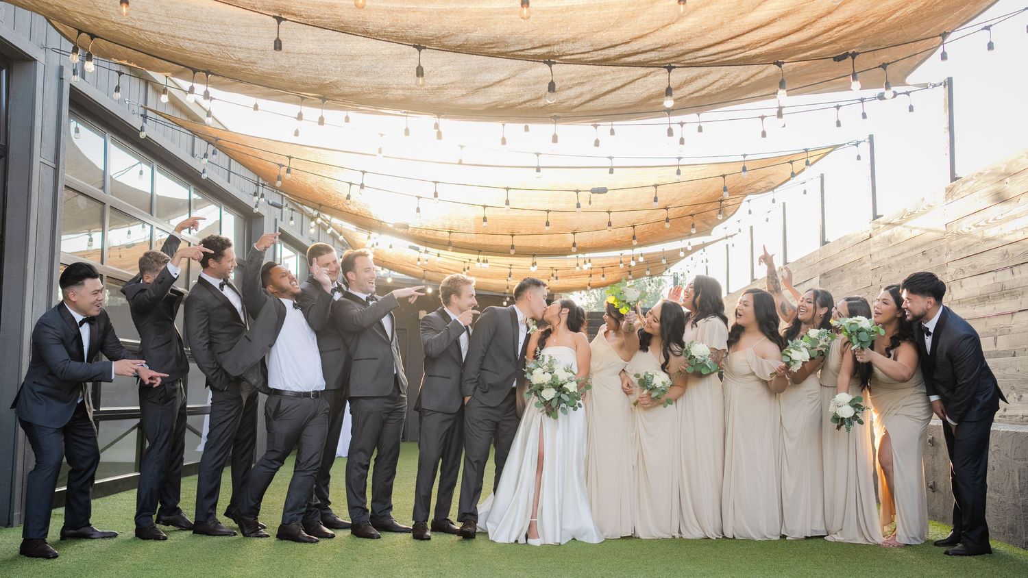 Wedding party lined up under draped fabric ceiling with string lights.