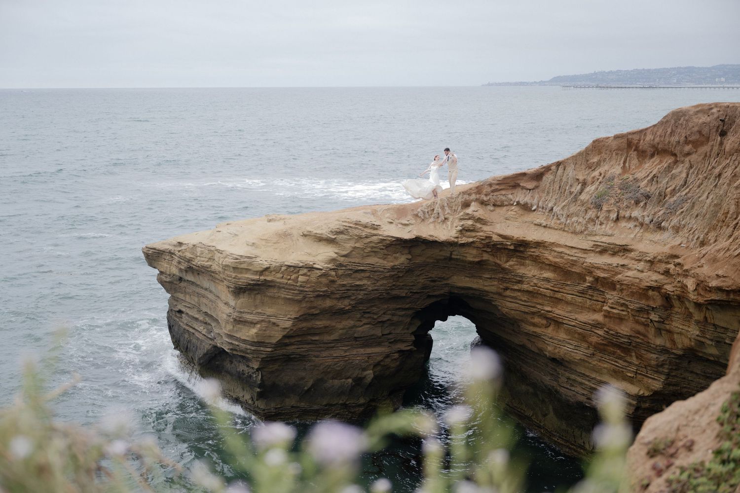 A scenic shot of a natural rock arch formation with a distant figure on top.