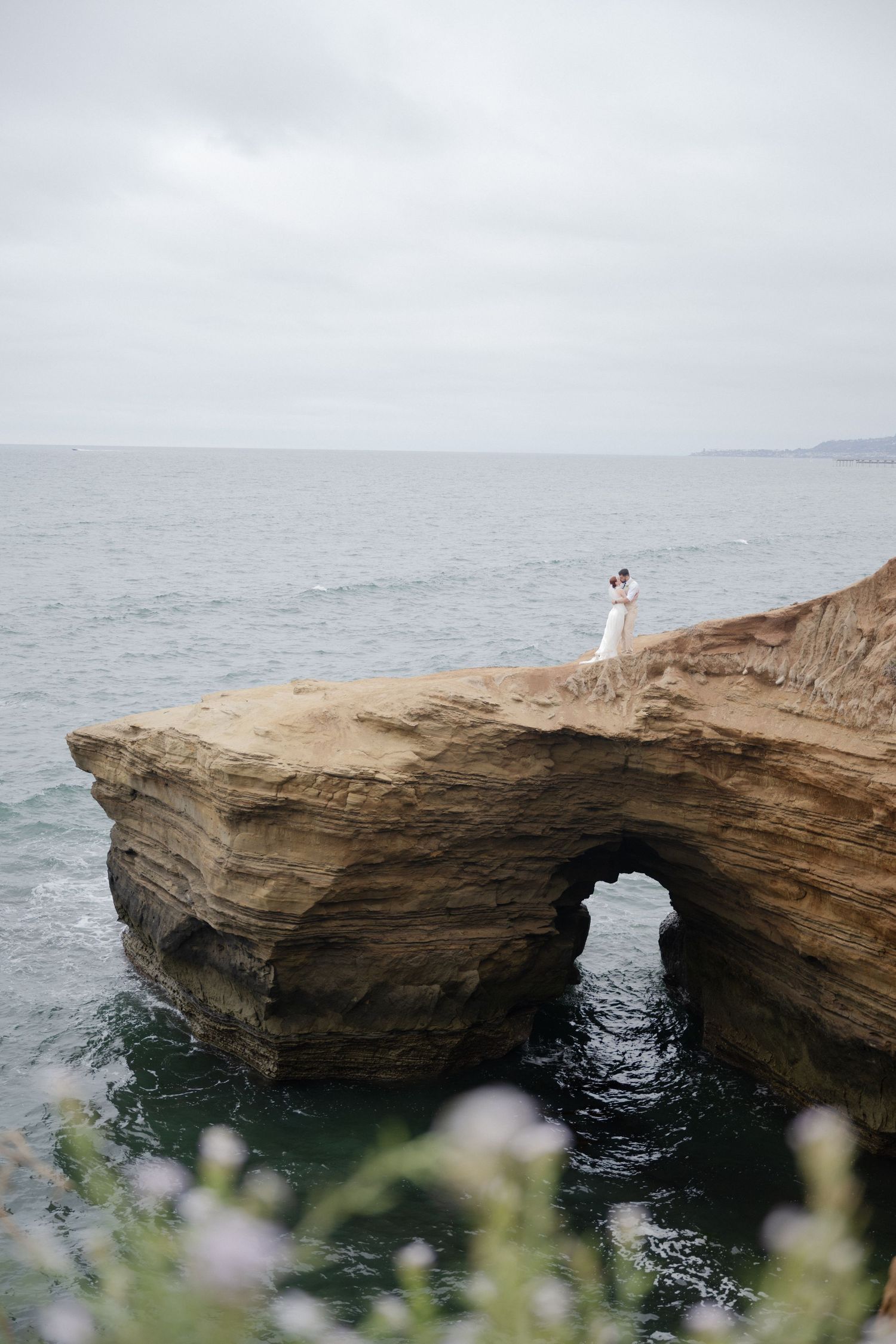 A white-clad figure stands atop a natural stone arch formation over the ocean.