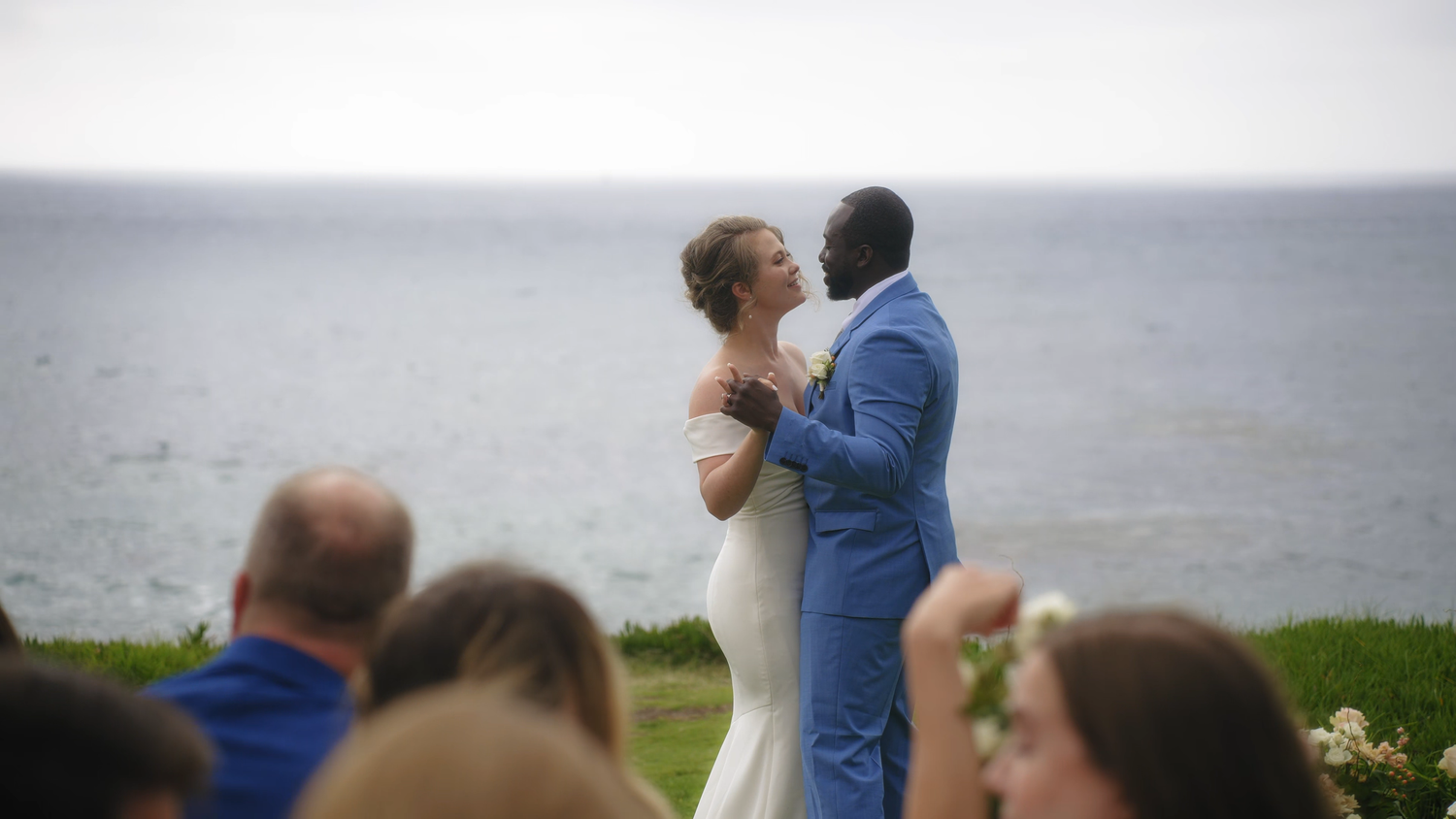 An oceanside wedding ceremony with guests watching the couple exchange vows.