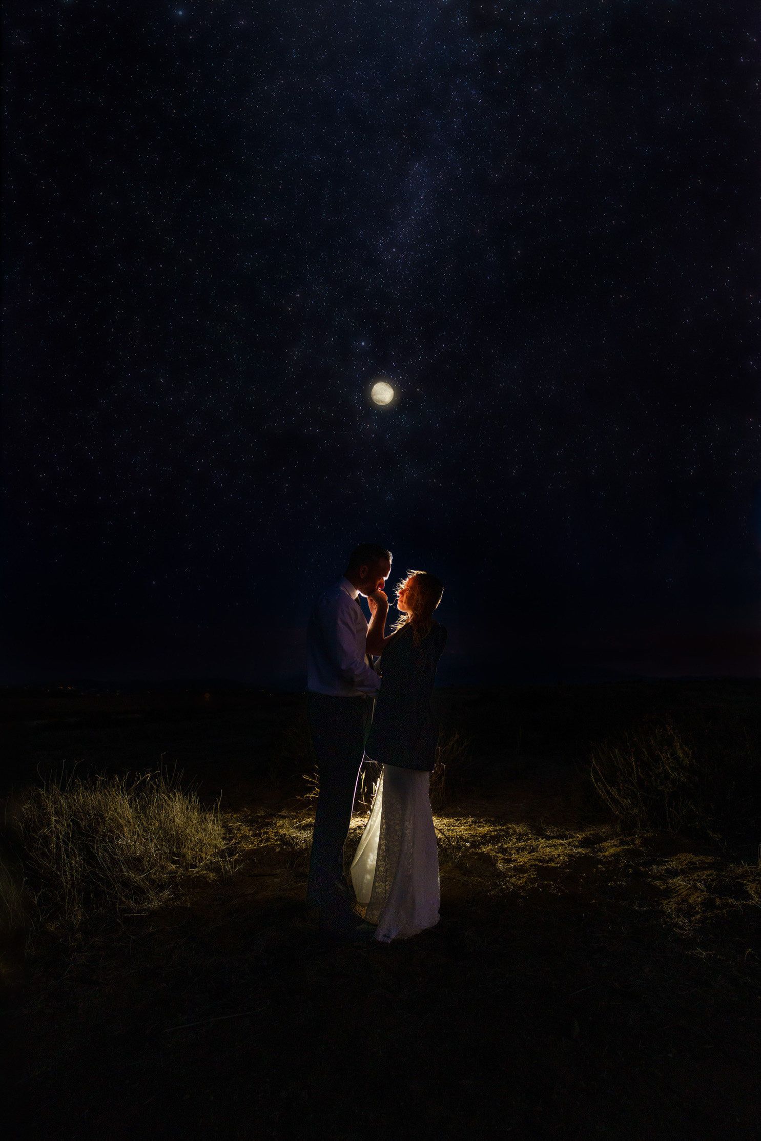A couple embracing under moonlit sky in dark desert landscape.