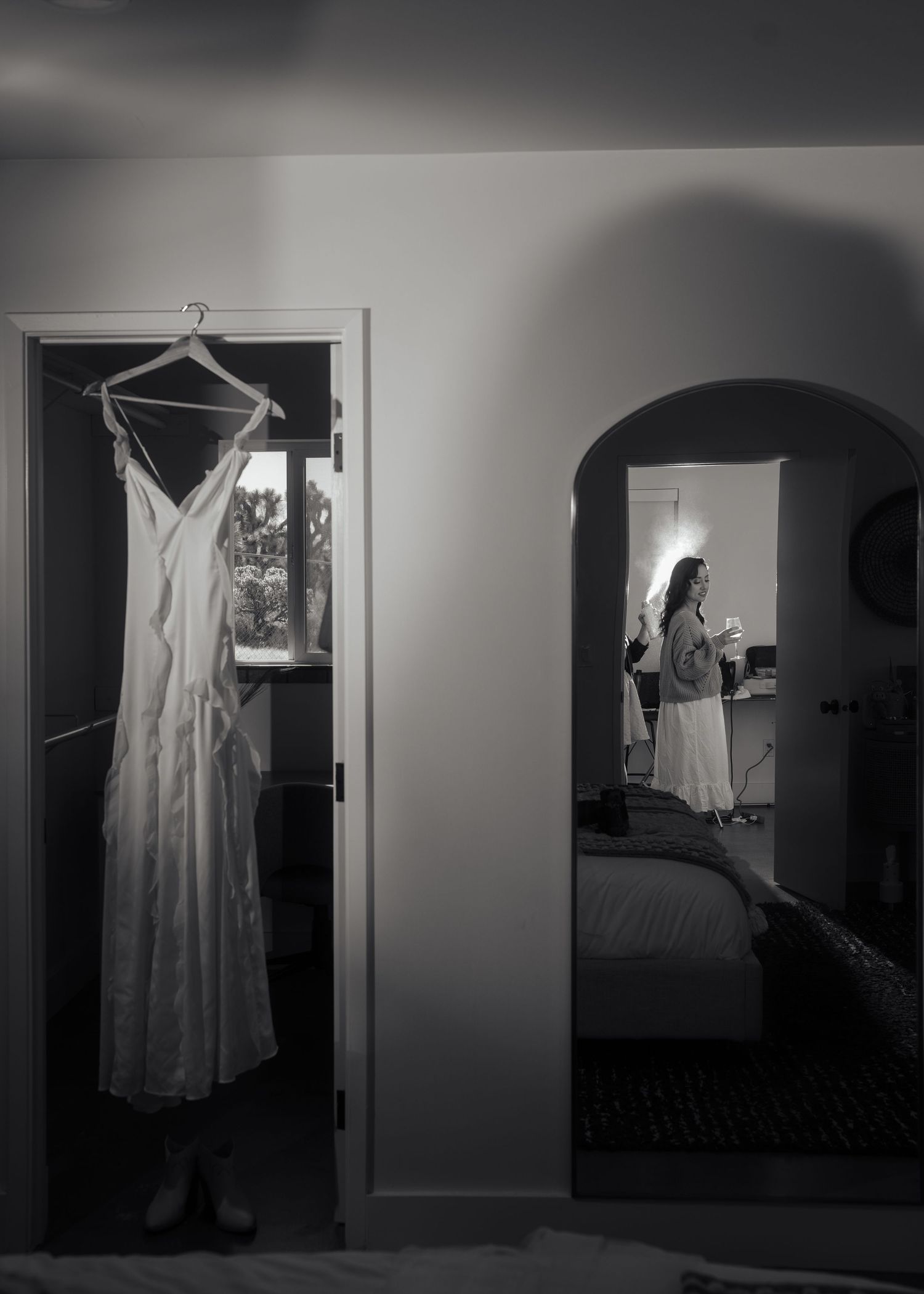 Wedding dress hanging in doorway with soft window light in black and white.