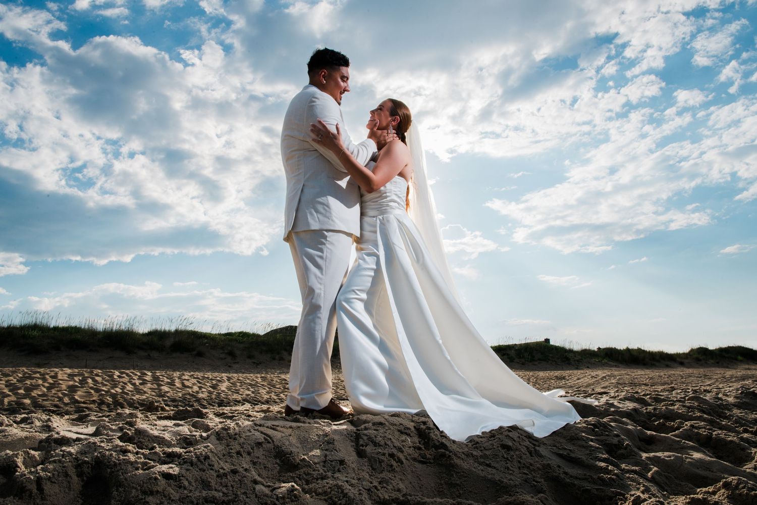 Bride and groom share romantic moment on rocky beach under dramatic cloudy sky.