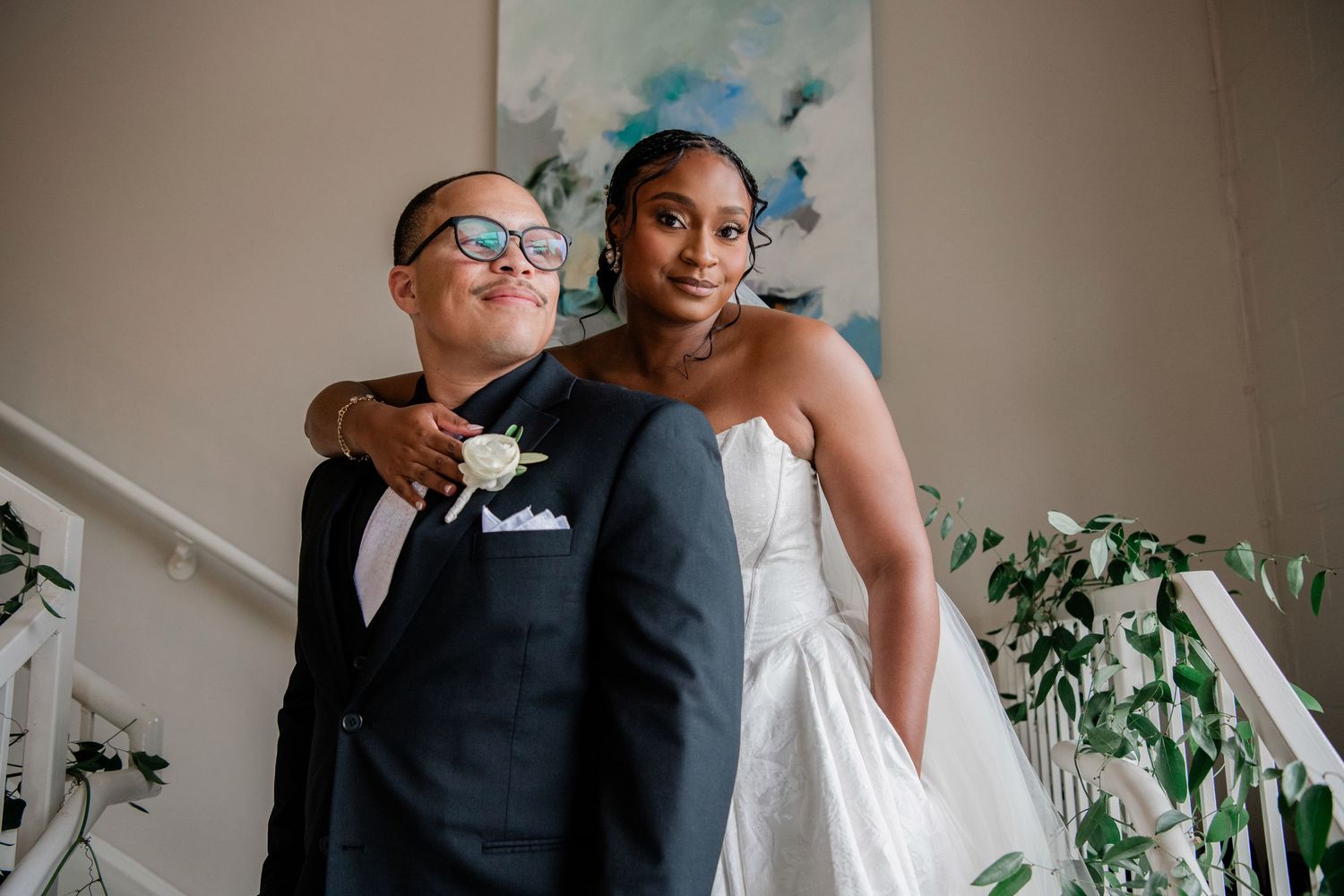 Bride and groom share tender moment on staircase, groom wearing boutonniere in tuxedo.