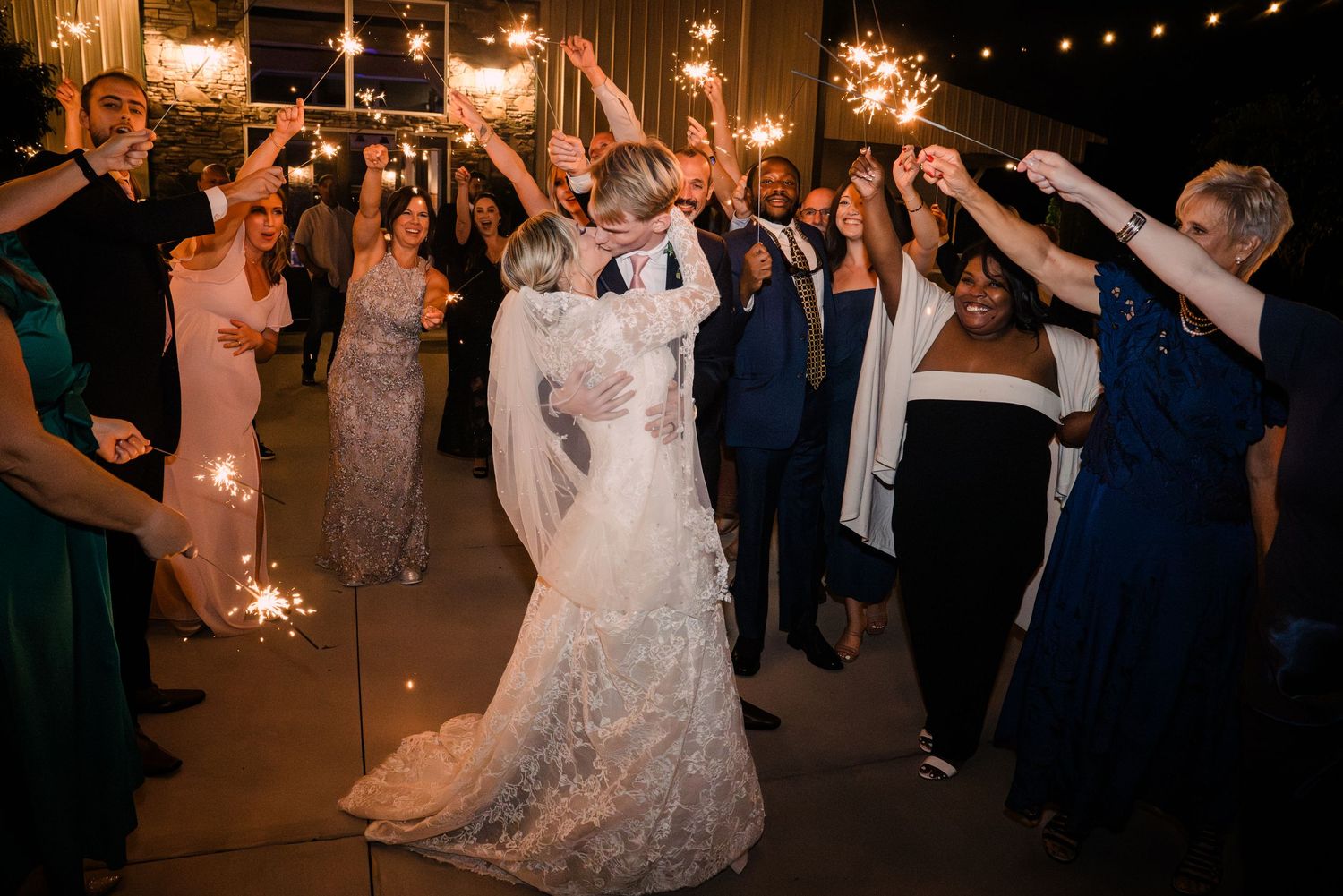 Bride and groom share romantic dance surrounded by guests holding sparklers at outdoor wedding reception.