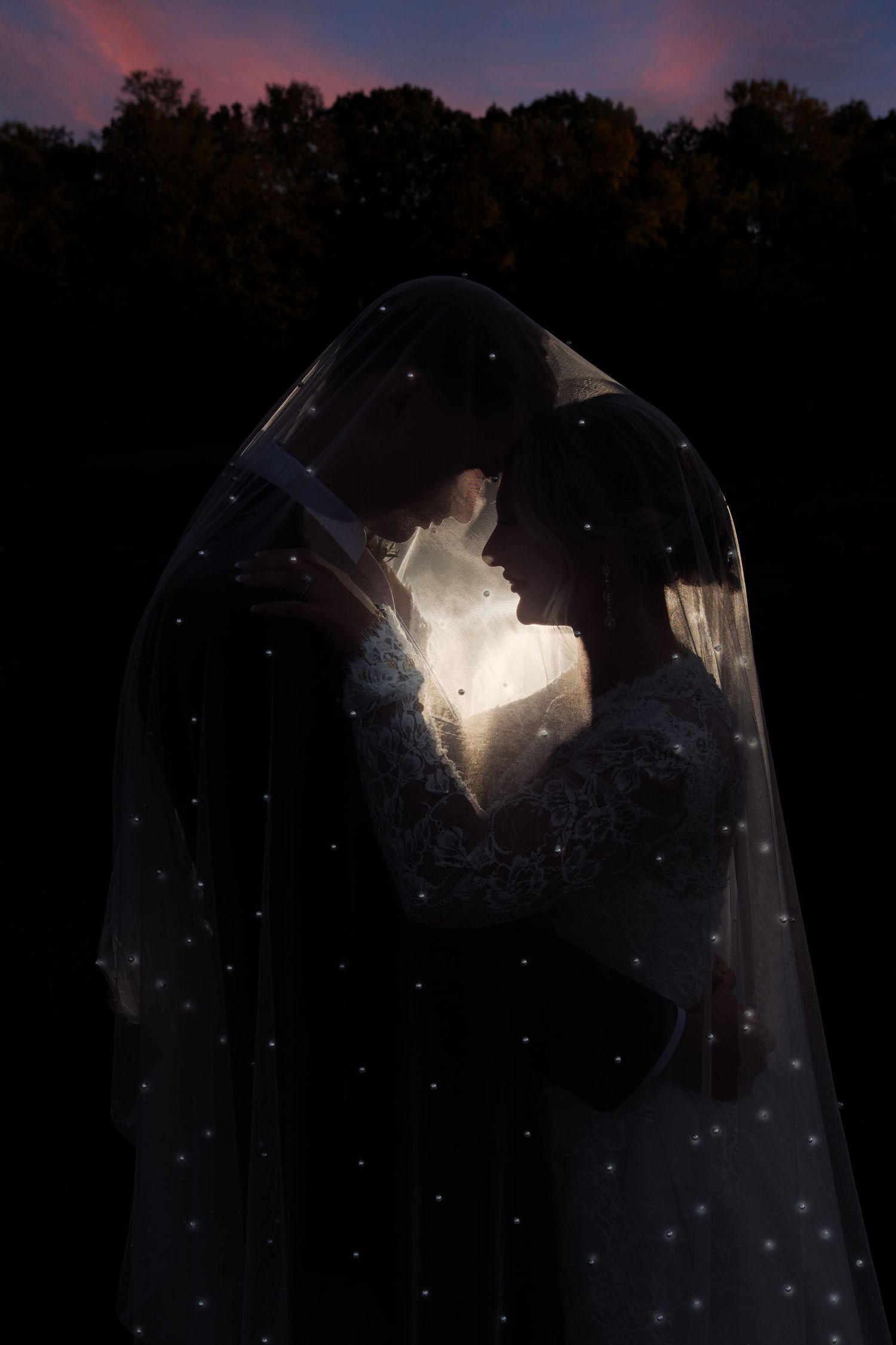 Romantic silhouette of bride and groom under starry veil glowing at twilight.