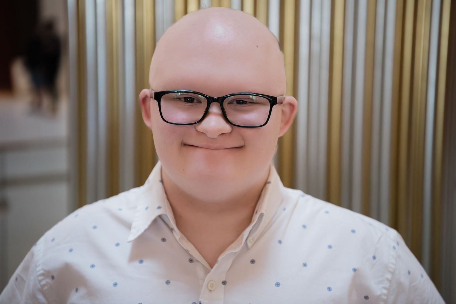 Smiling bald man wearing glasses and white polka dot shirt poses for portrait indoors.