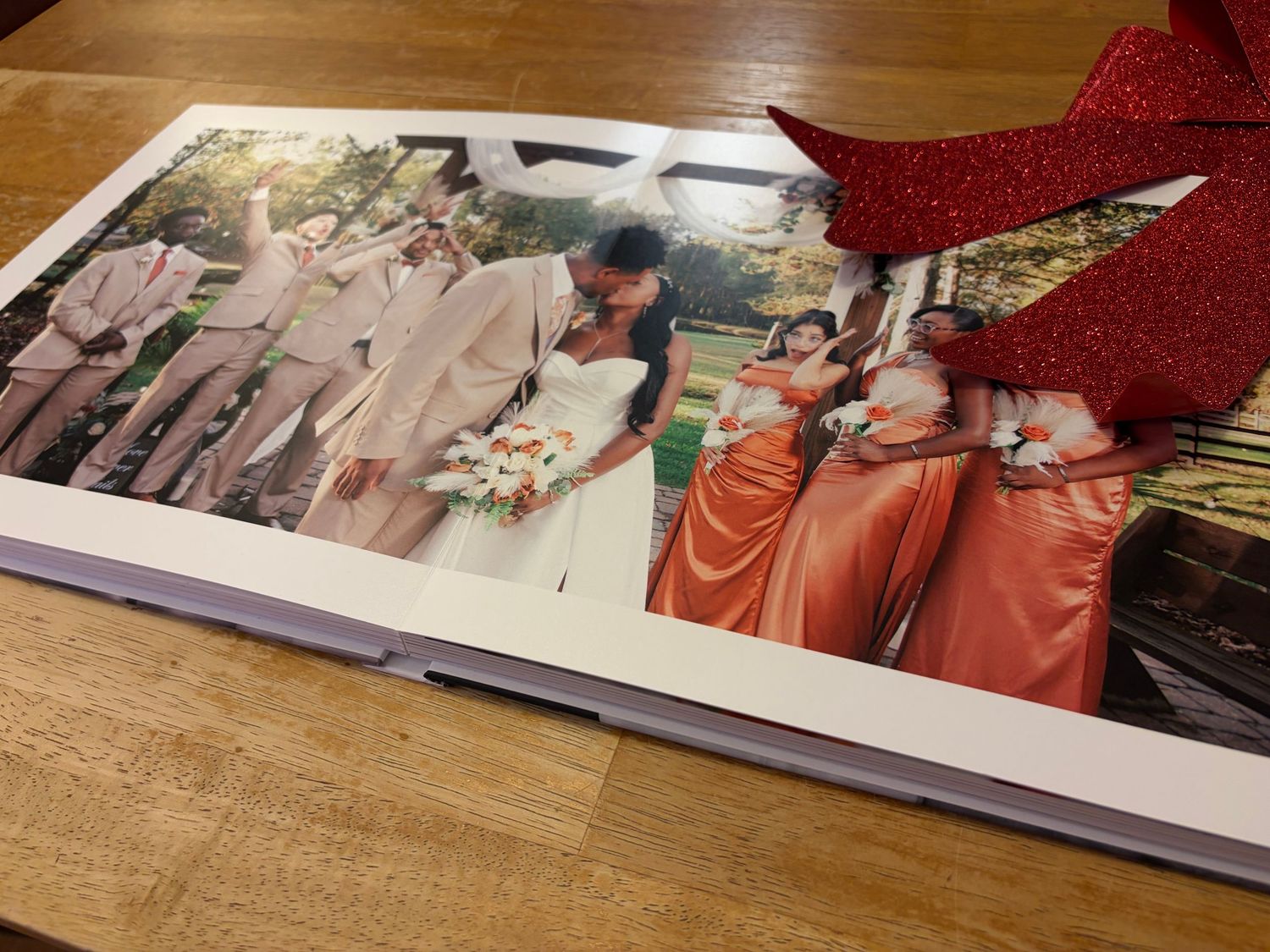 Open wedding photo album on table showing bride and groom kissing with bridesmaids in orange dresses.