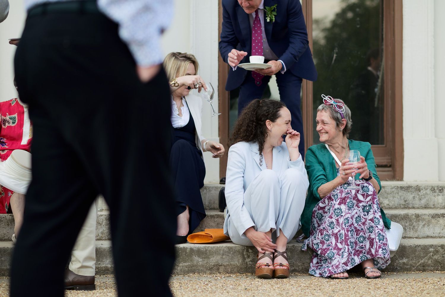 A group of wedding guests sit on stone steps outside a building during a formal celebration.