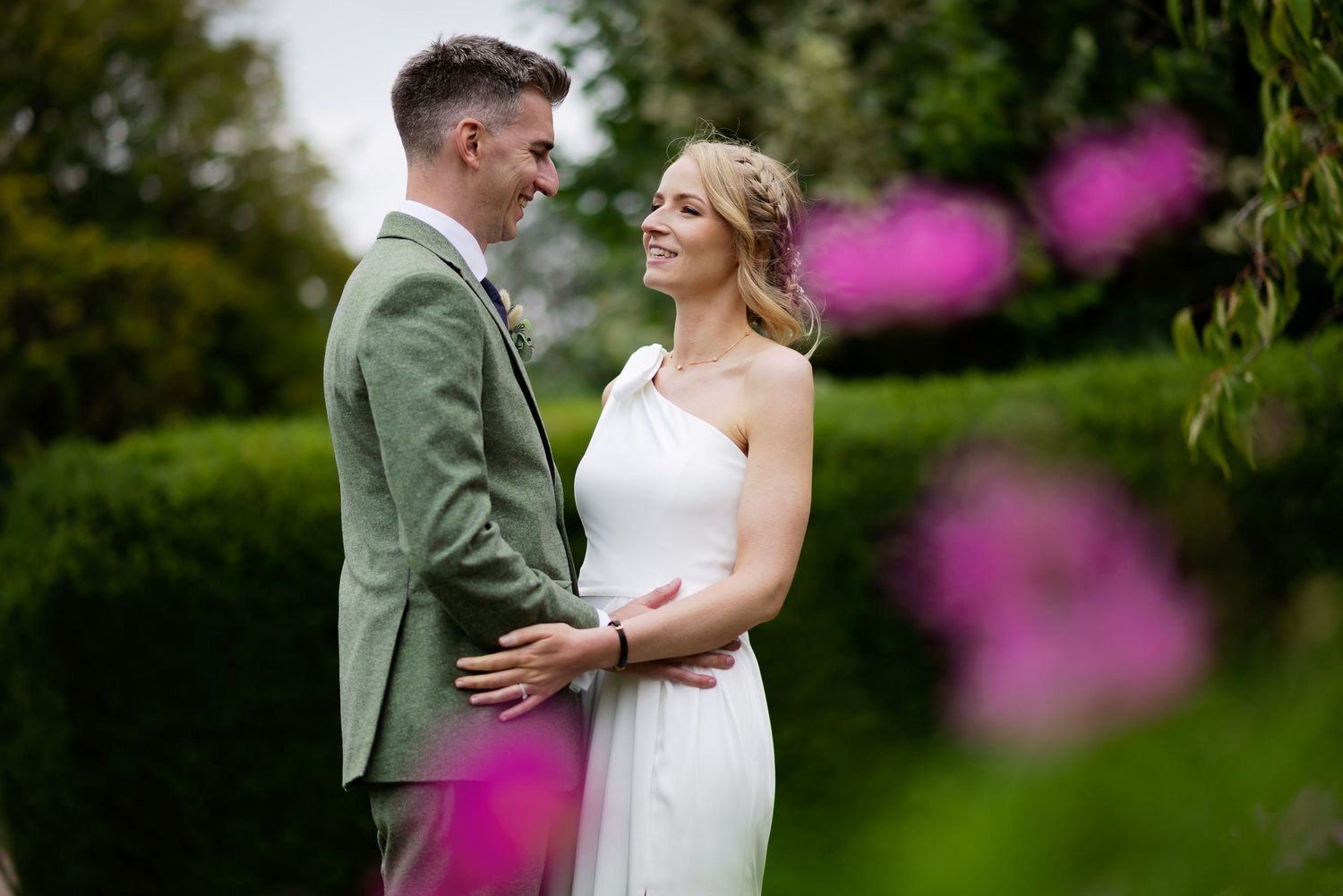 Elegant garden wedding portrait with pink flowers in soft focus foreground.