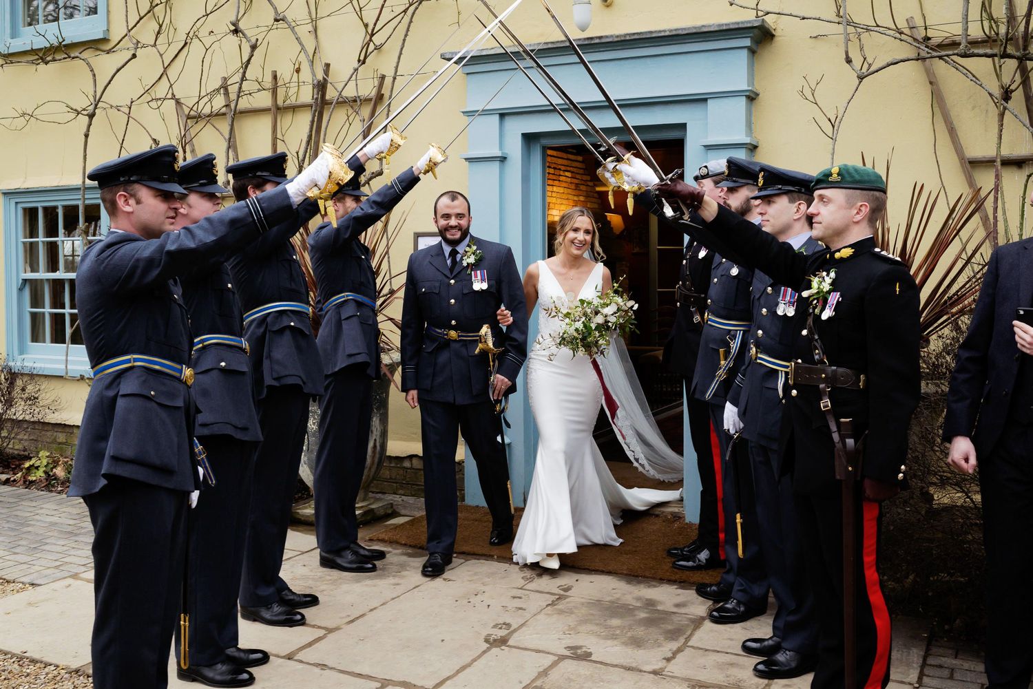 Military honor guard forms sword arch for couple exiting historic building after ceremony.