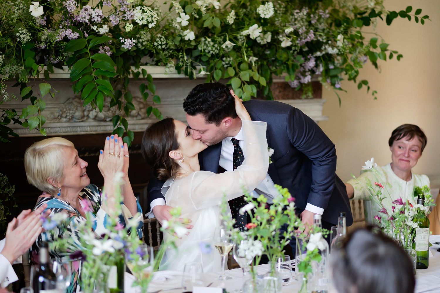 Wedding reception table decorated with white floral arrangements as couple shares intimate moment.