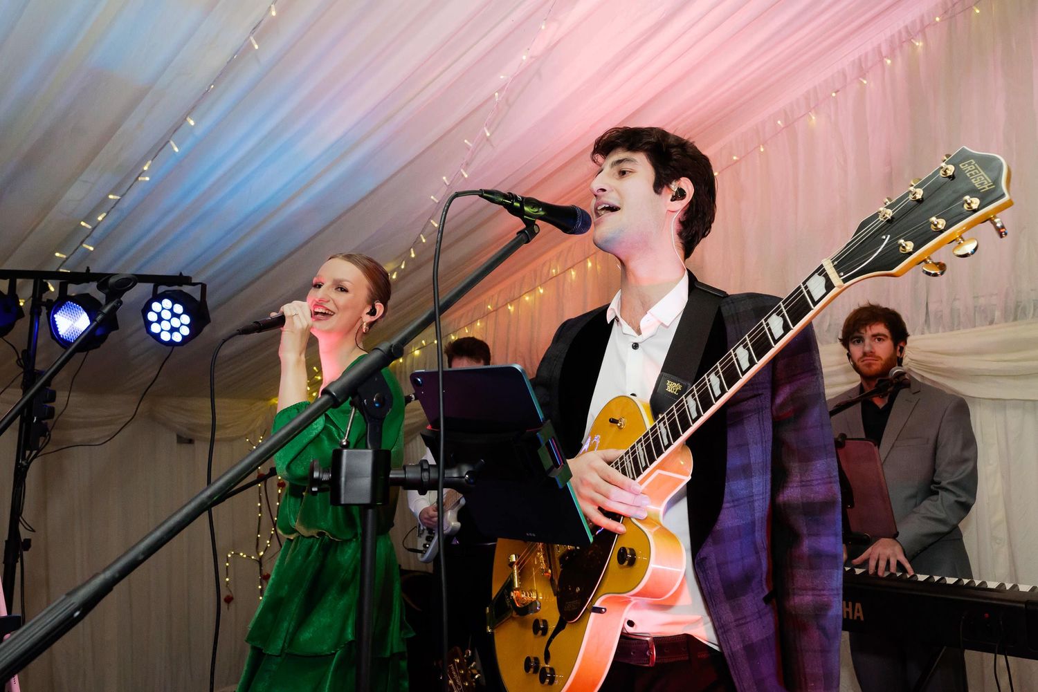 Live band performing on stage with guitarist and vocalist under colorful lighting.