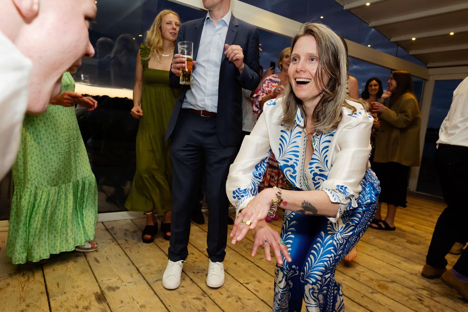 Casual party scene with guests dancing on wooden floor under string lights.
