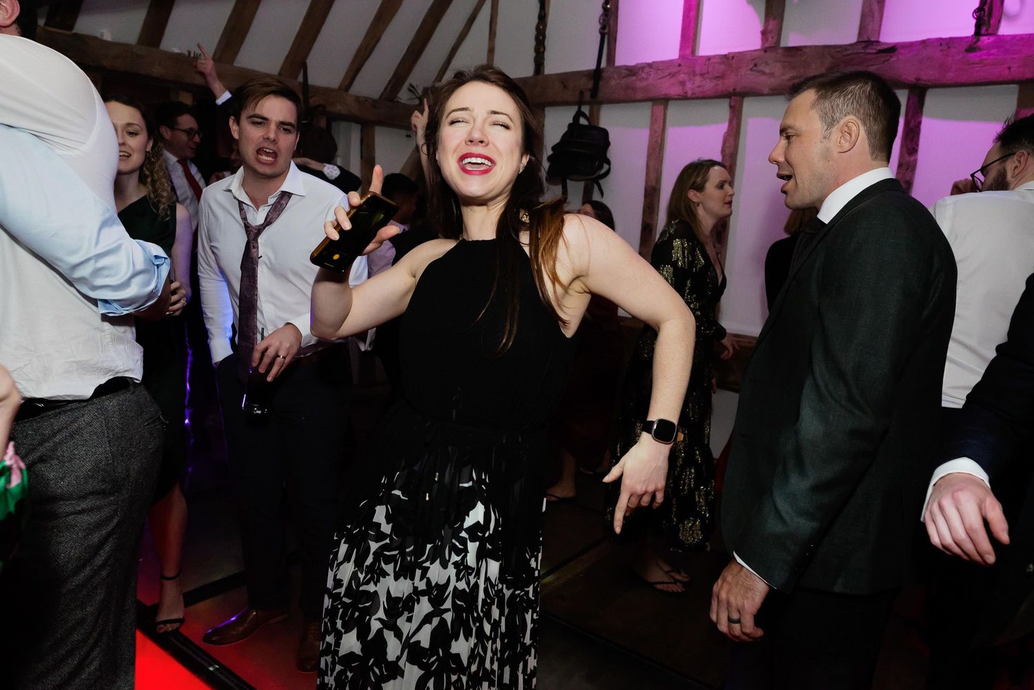 A guest dances exuberantly at a wedding reception under pink mood lighting.