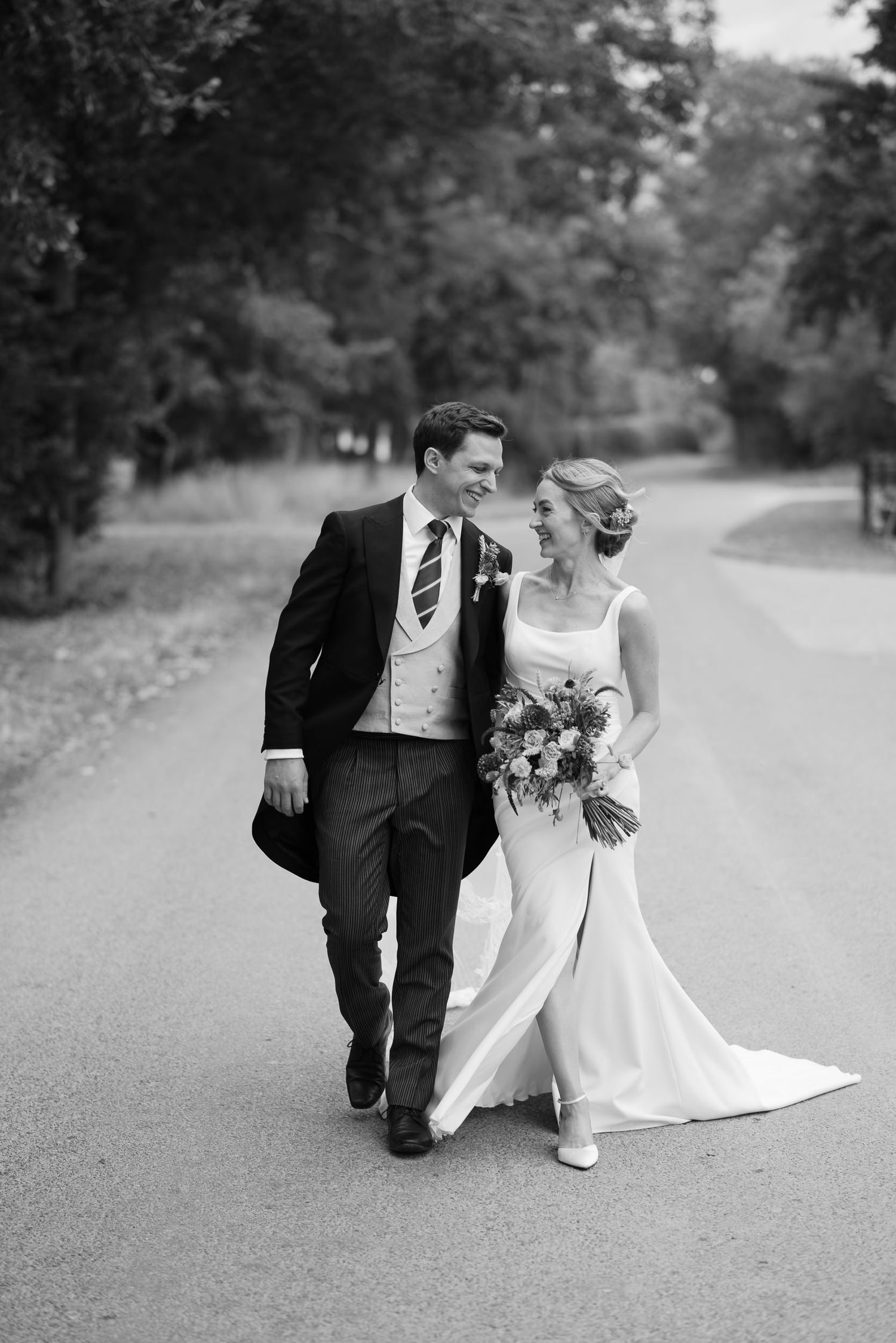 A series of black and white wedding photos showing a couple walking and posing together on a tree-lined path.
