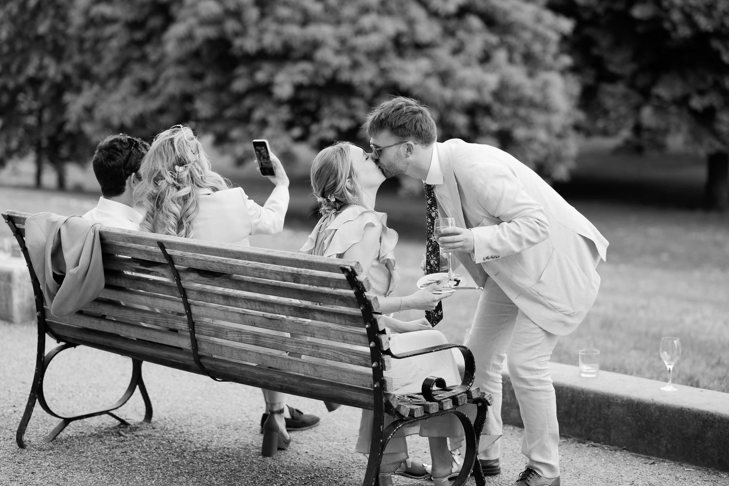 Black and white photo of people interacting on a park bench outdoors.