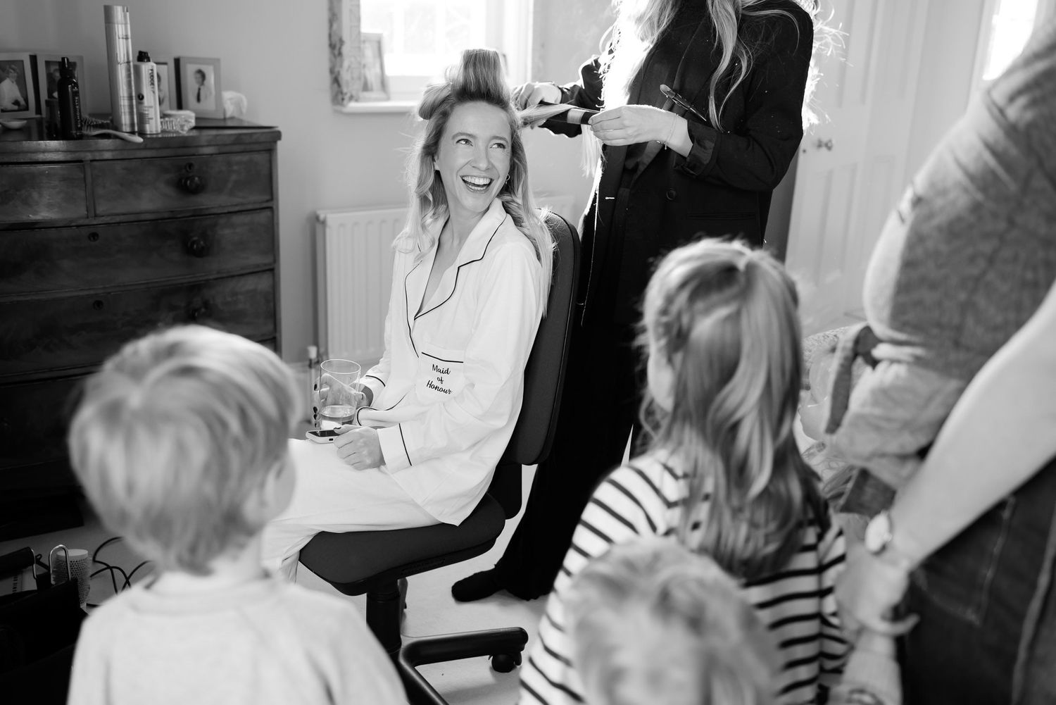 Candid black and white photo of morning preparations with children watching.