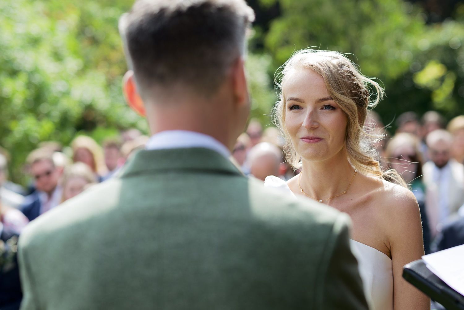 A wedding ceremony in a garden setting with guests gathered around as the couple exchanges vows.