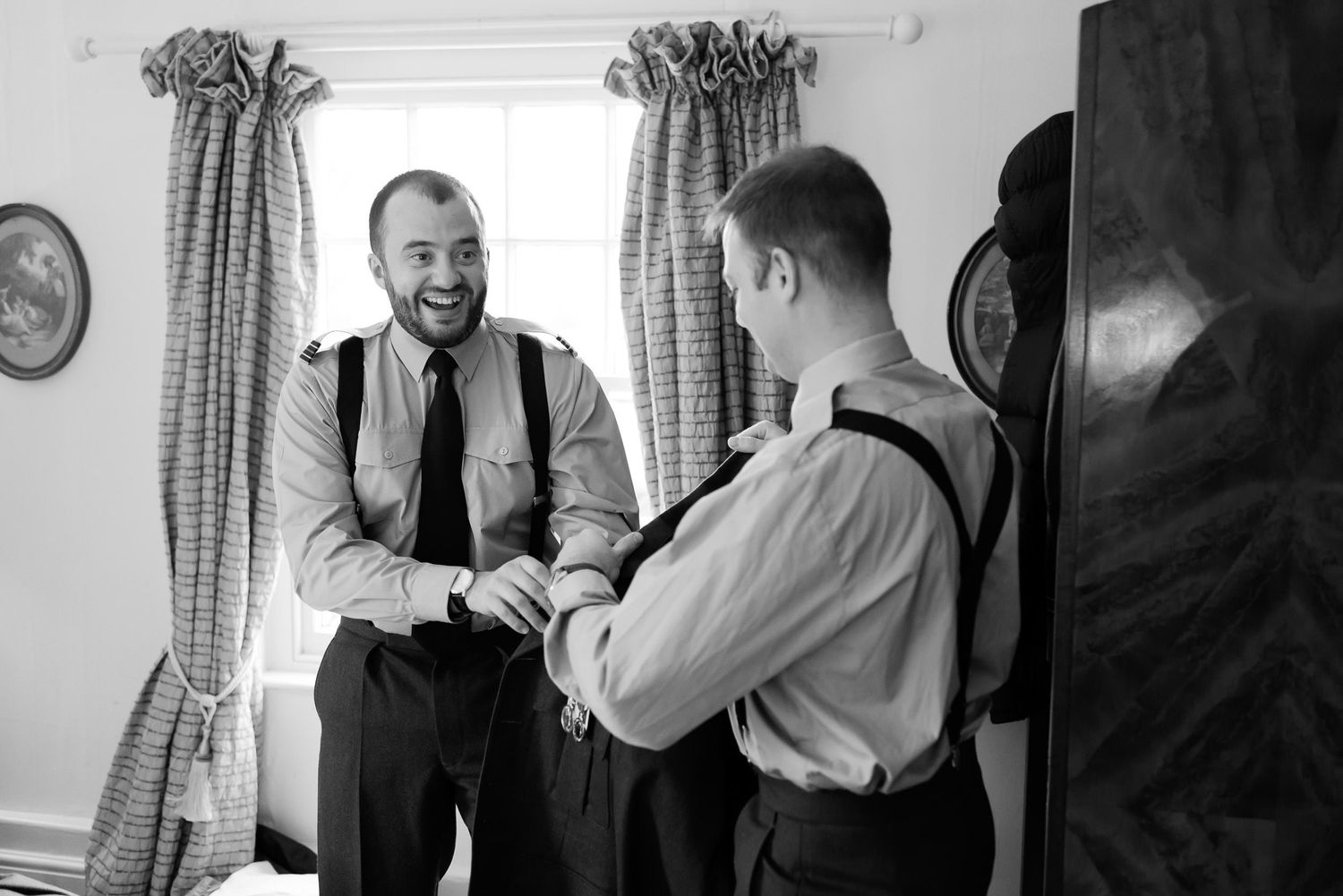 Groomsmen sharing a laughing moment while getting dressed in formal attire.