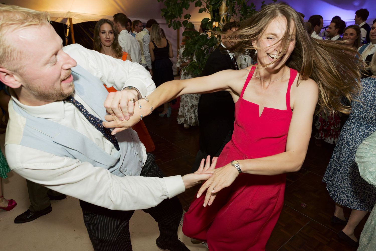 Two people energetically dancing together at a party, with one wearing a red dress and the other in white.