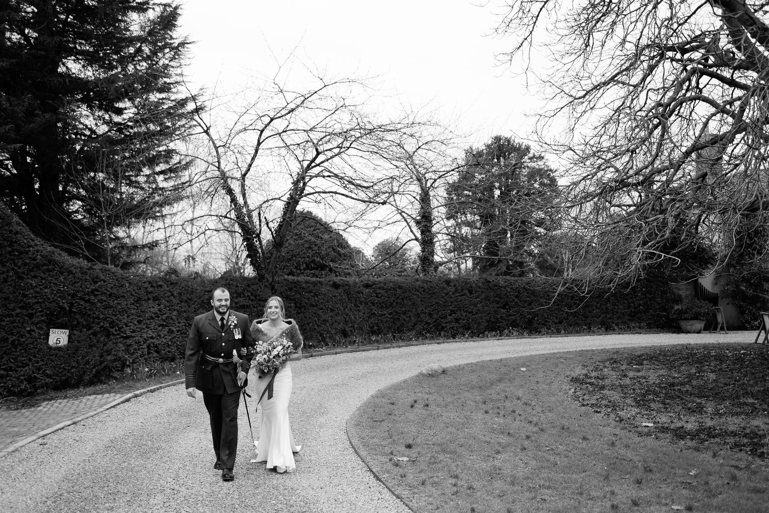 Black and white photo of couple walking along curved garden path surrounded by trees.