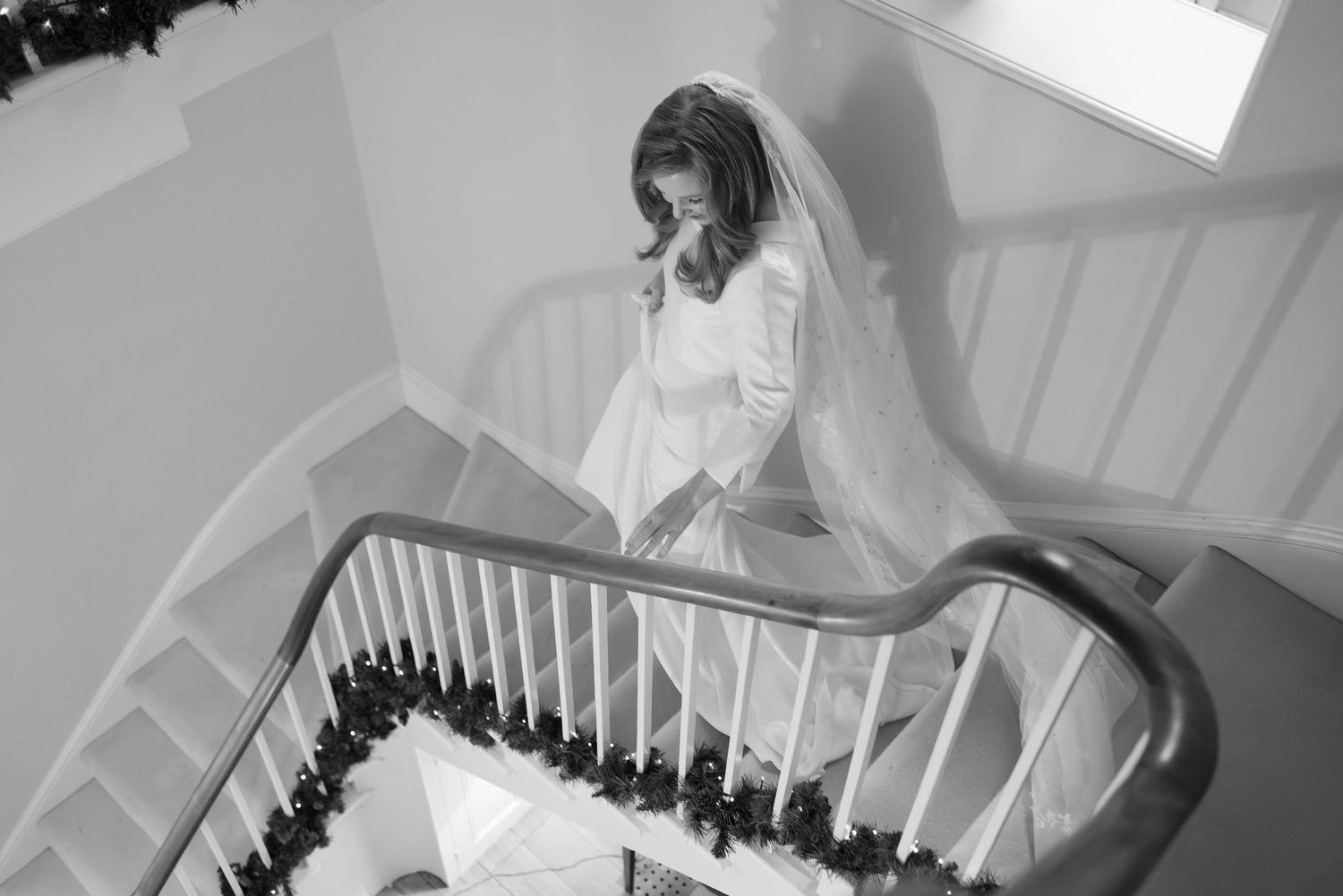Black and white view of wedding party walking down grand staircase in formal wear.