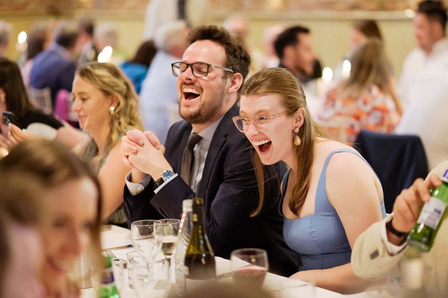 Reception guests sharing genuine laughter at wedding celebration dinner.
