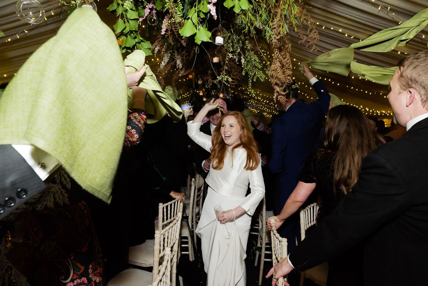 Wedding guests gathered under decorative greenery and floral arrangements at an indoor reception.