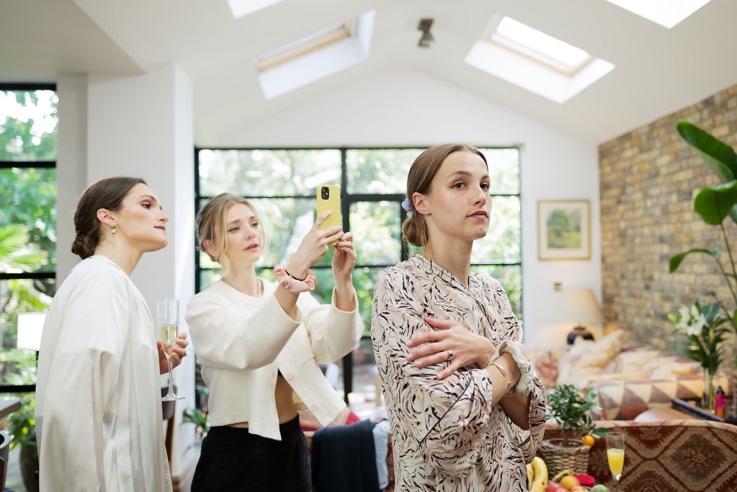 Women in robes prepare for a wedding while getting ready in a sunlit room with skylights.
