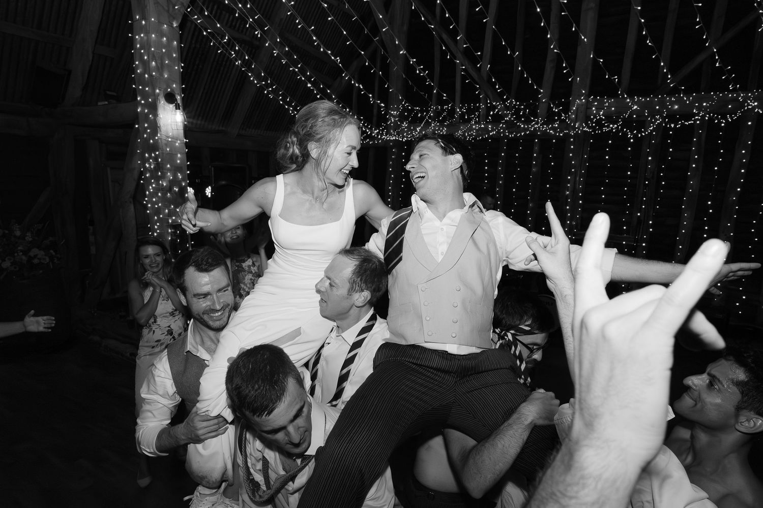 Wedding guests lift and celebrate during a lively dance party under twinkling lights.