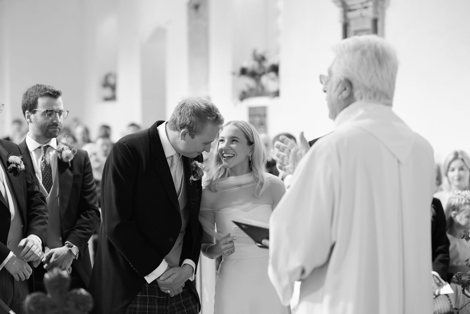 Black and white photos of wedding ceremony moments in a church with guests and clergy.