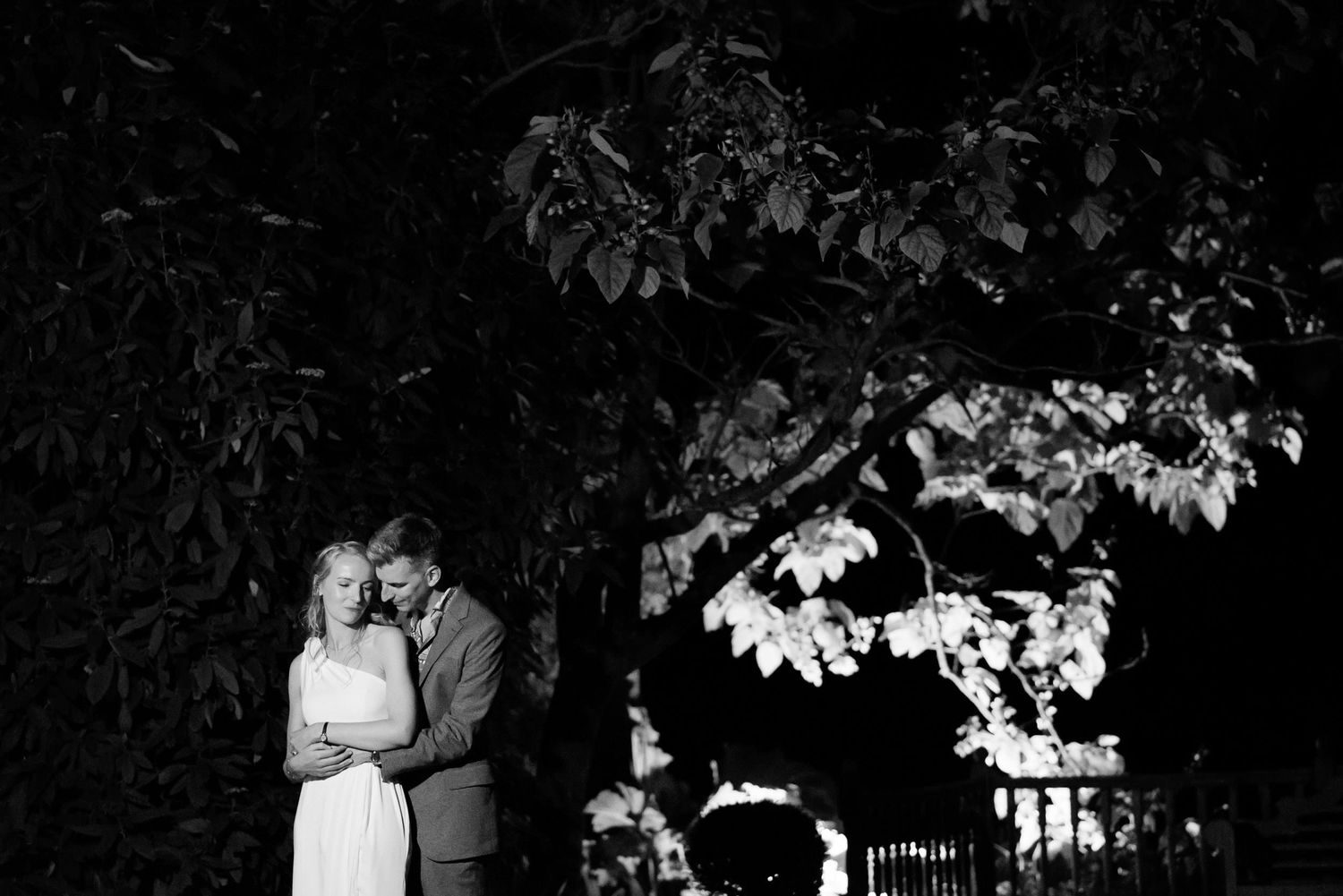 Romantic nighttime portrait of couple under tree branches in black and white.