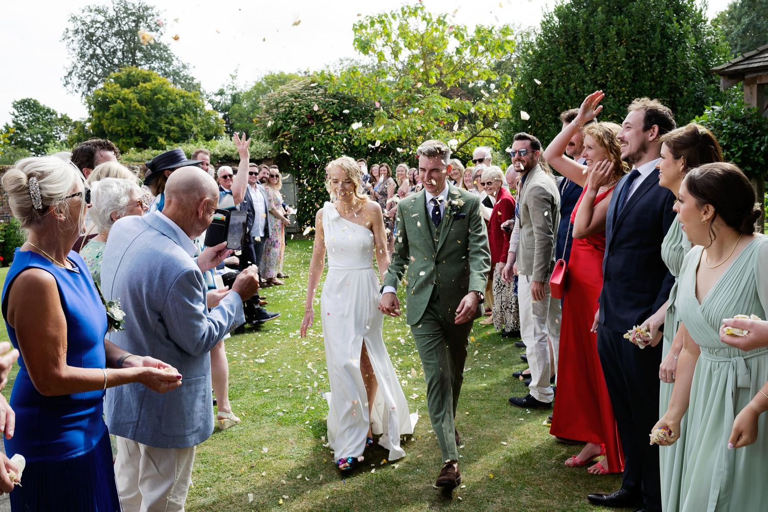 Wedding guests form an aisle outdoors while celebrating the newlyweds' procession.