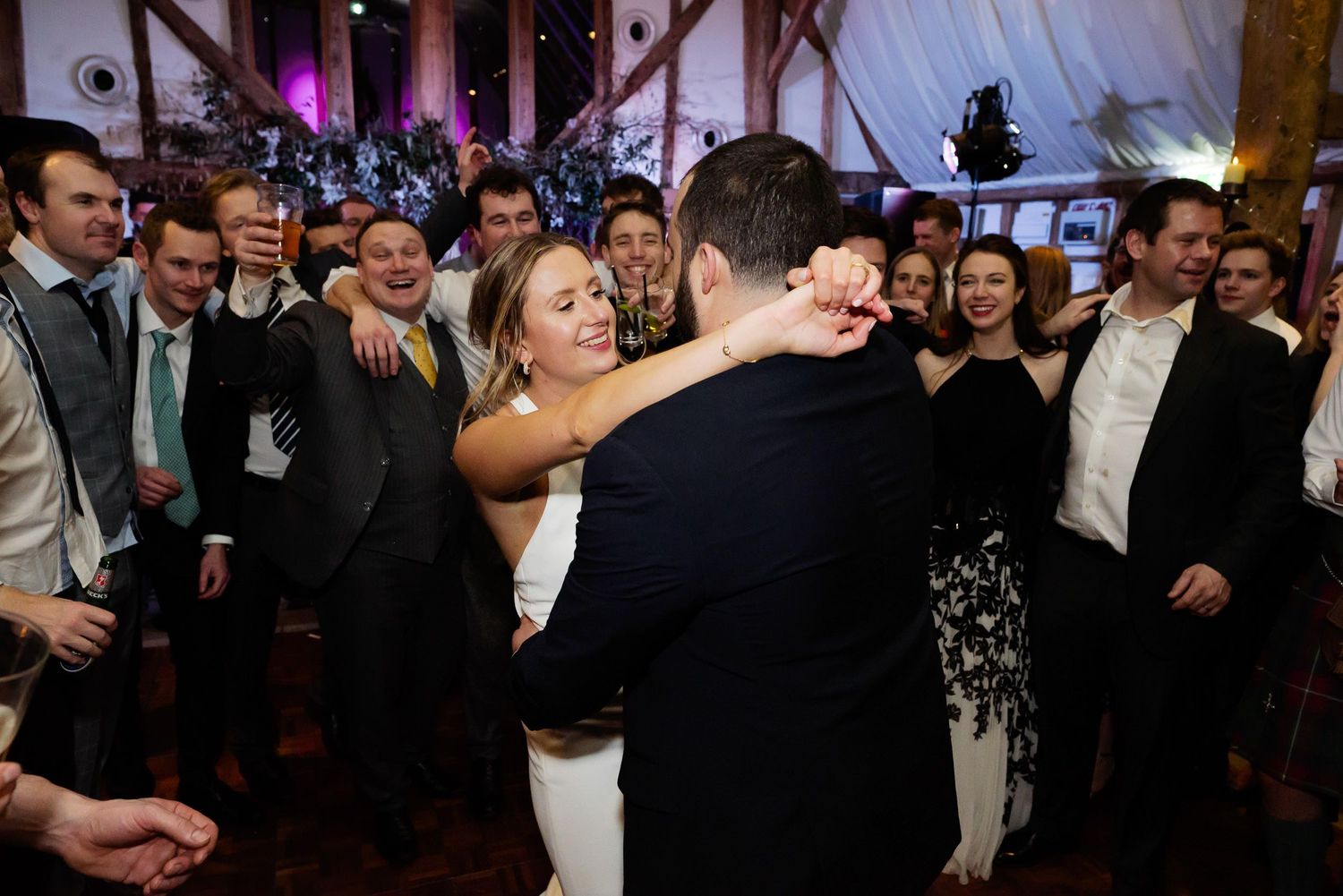Wedding couple dancing surrounded by guests at evening reception celebration.