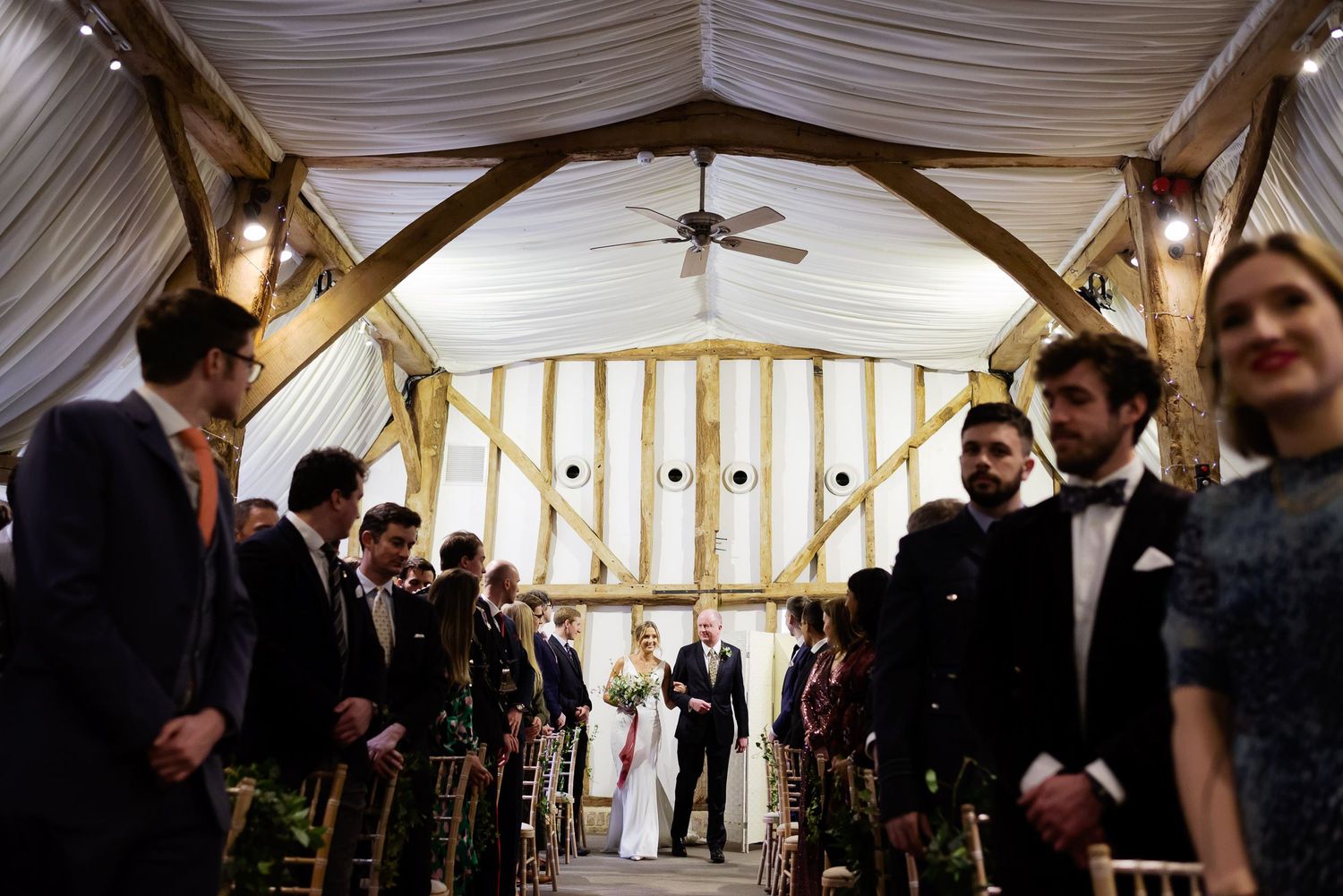 Wedding ceremony in progress under wooden arch with draped fabric in intimate venue.