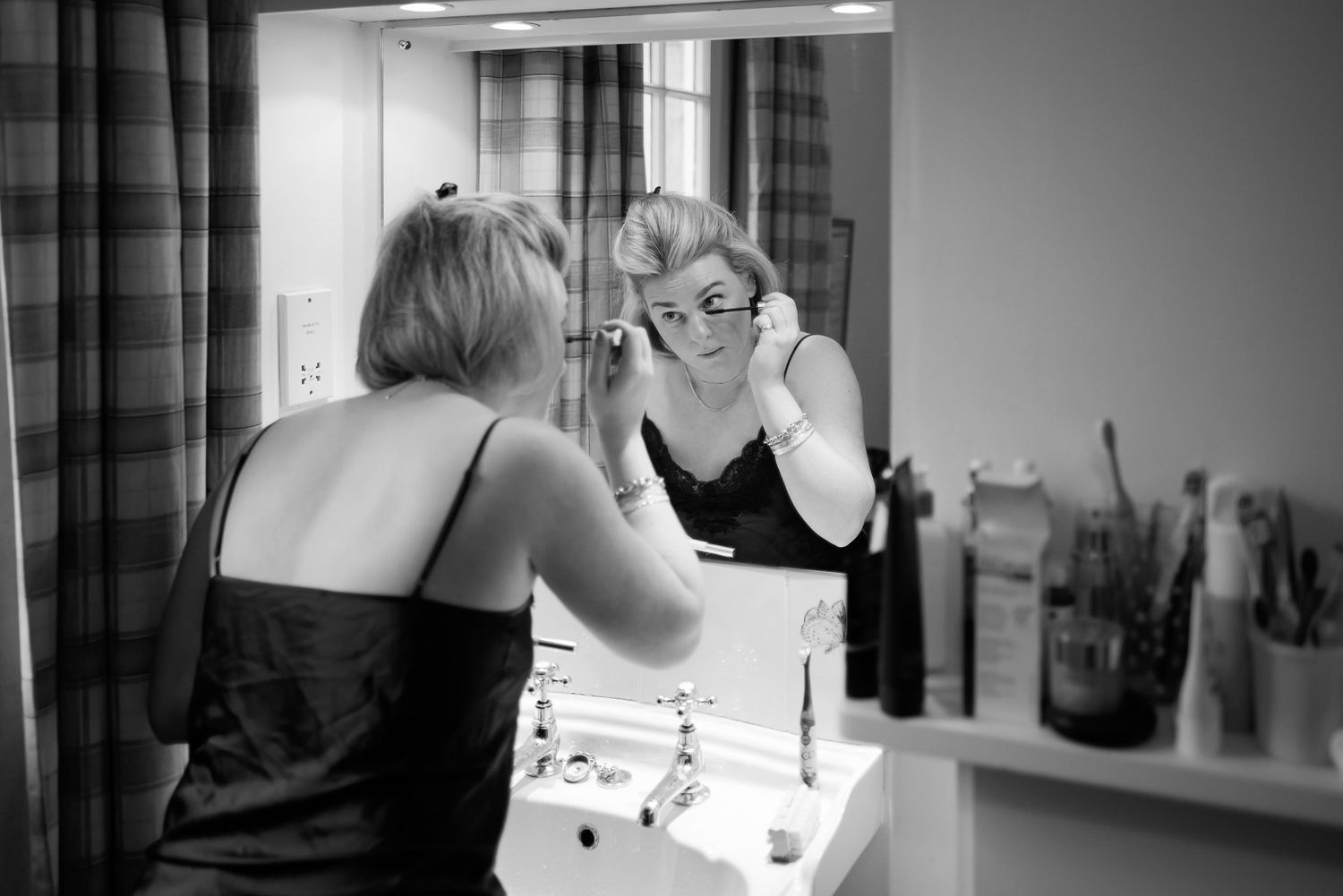 Black and white photo of wedding preparation at a vanity mirror.