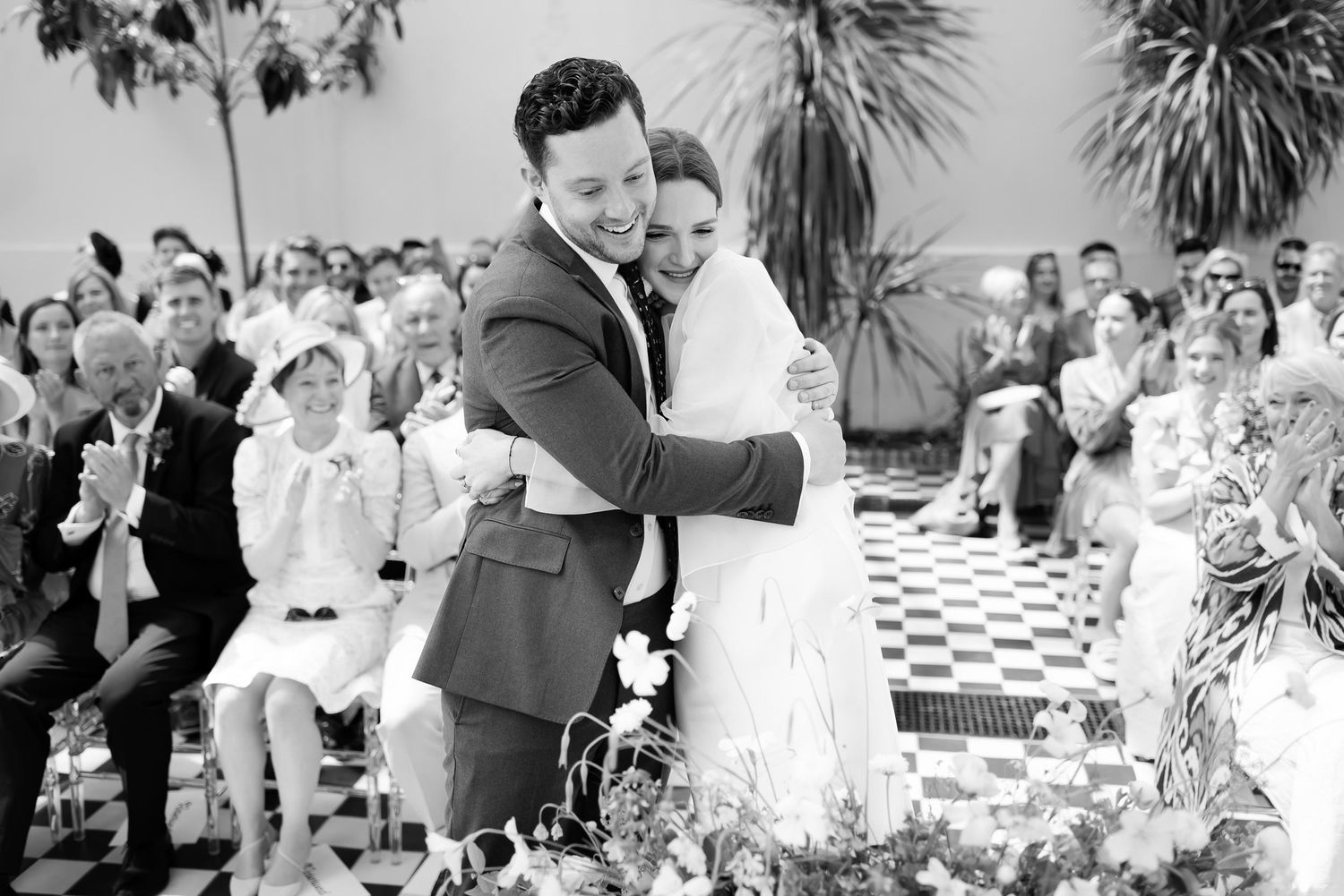 Newly married couple embracing during a joyful outdoor wedding ceremony on a checkered floor.
