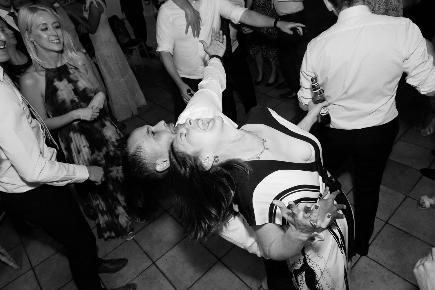 Party guests perform dynamic dance moves on a tiled floor at a celebration.