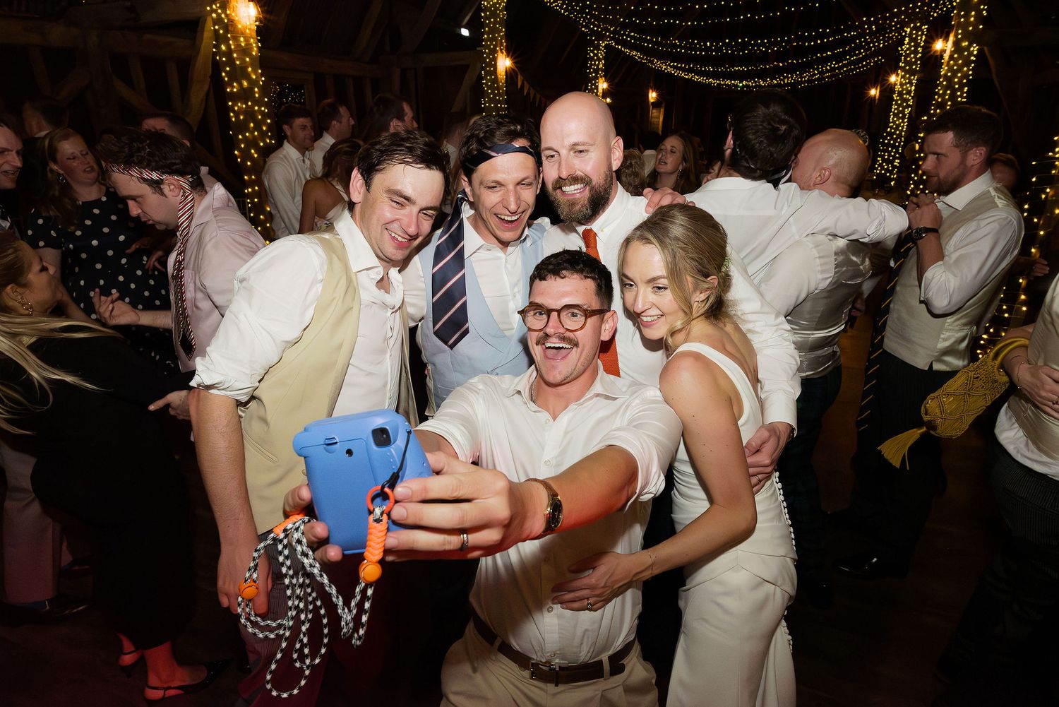 Wedding guests dancing and celebrating under ambient lighting at an indoor reception.