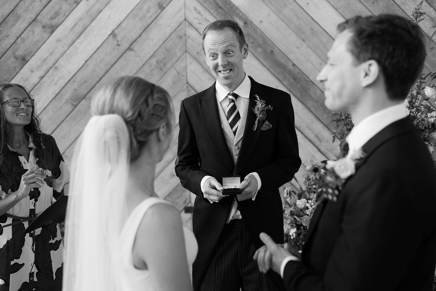 Wedding ceremony taking place in front of a rustic diagonal wood plank wall with floral arrangements.
